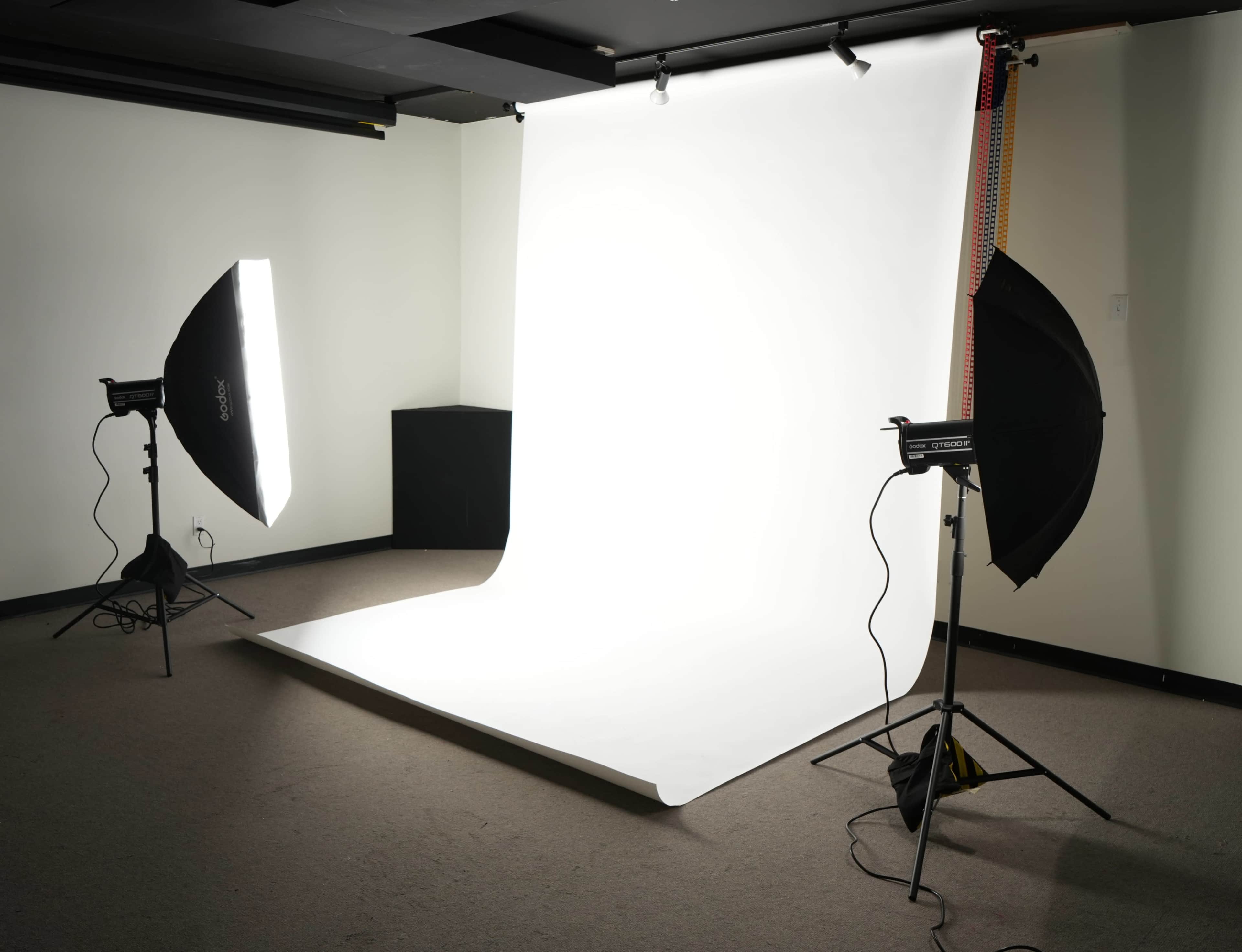 The image shows a photography studio setup with a white backdrop and two softbox lights positioned on either side.