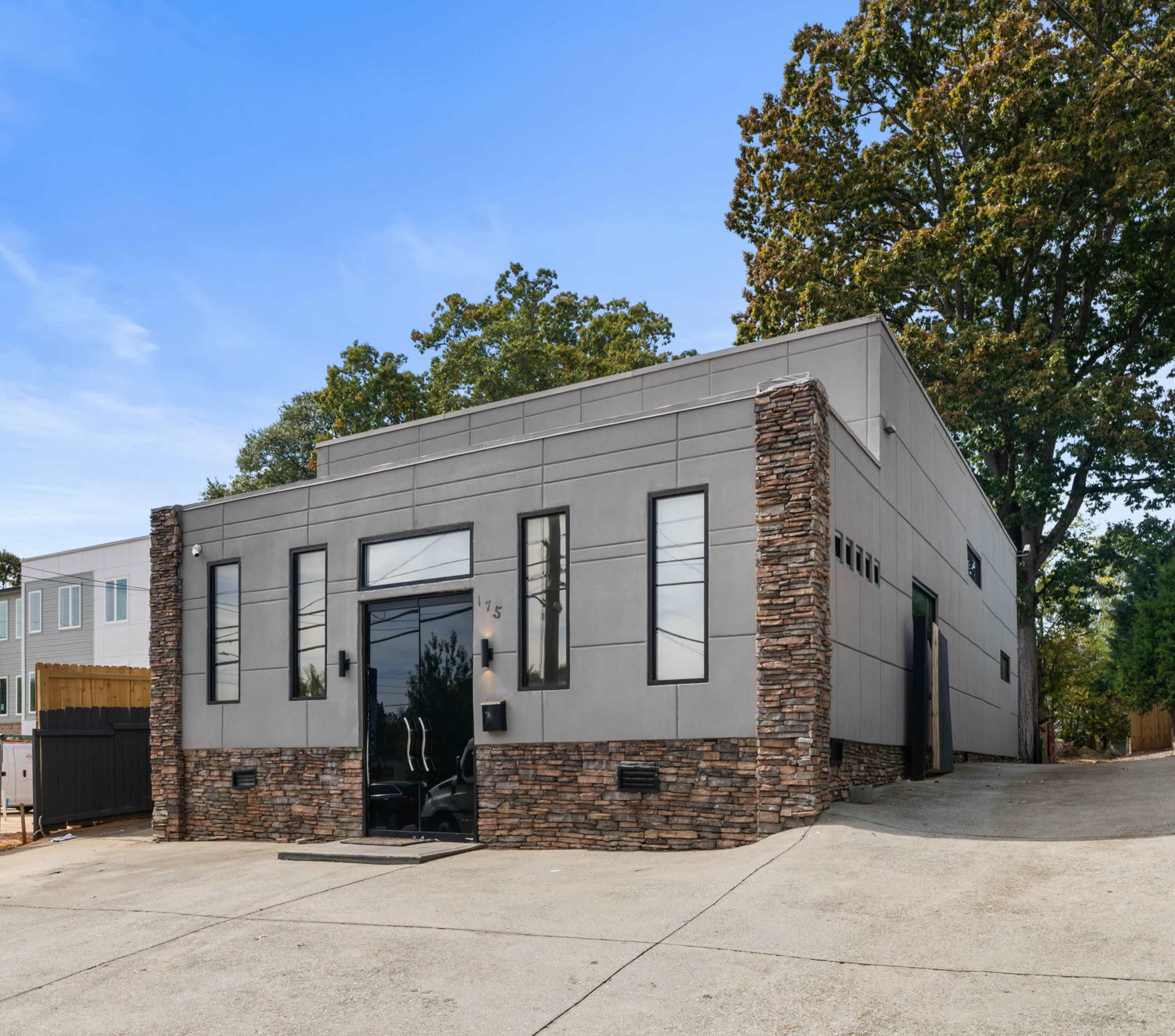 The image shows a modern gray building with stone accents on the front and a large glass entrance.
