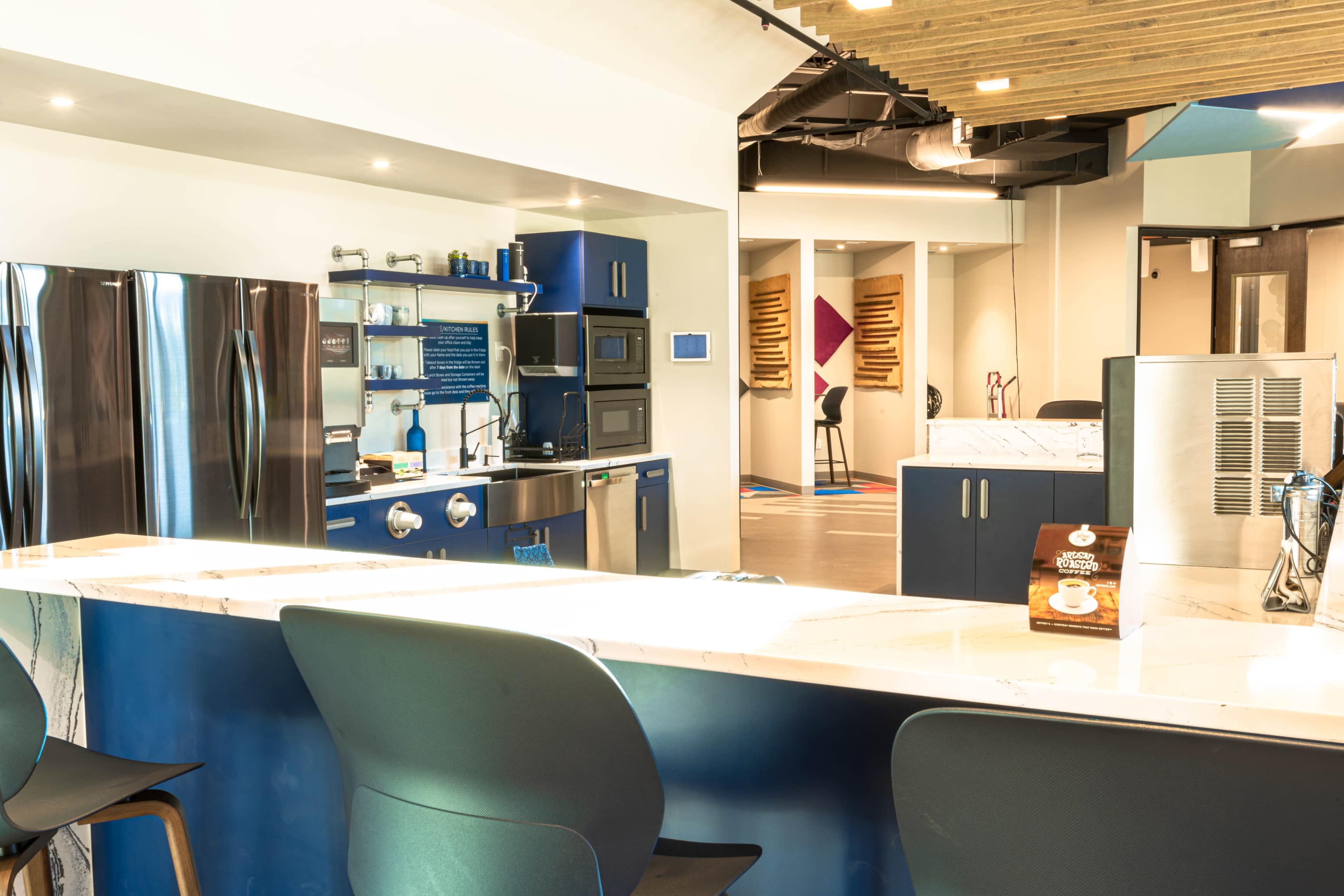 The image shows a modern kitchen area with stainless steel appliances, a marble countertop, and a colorful, open space featuring seating and varied decor.