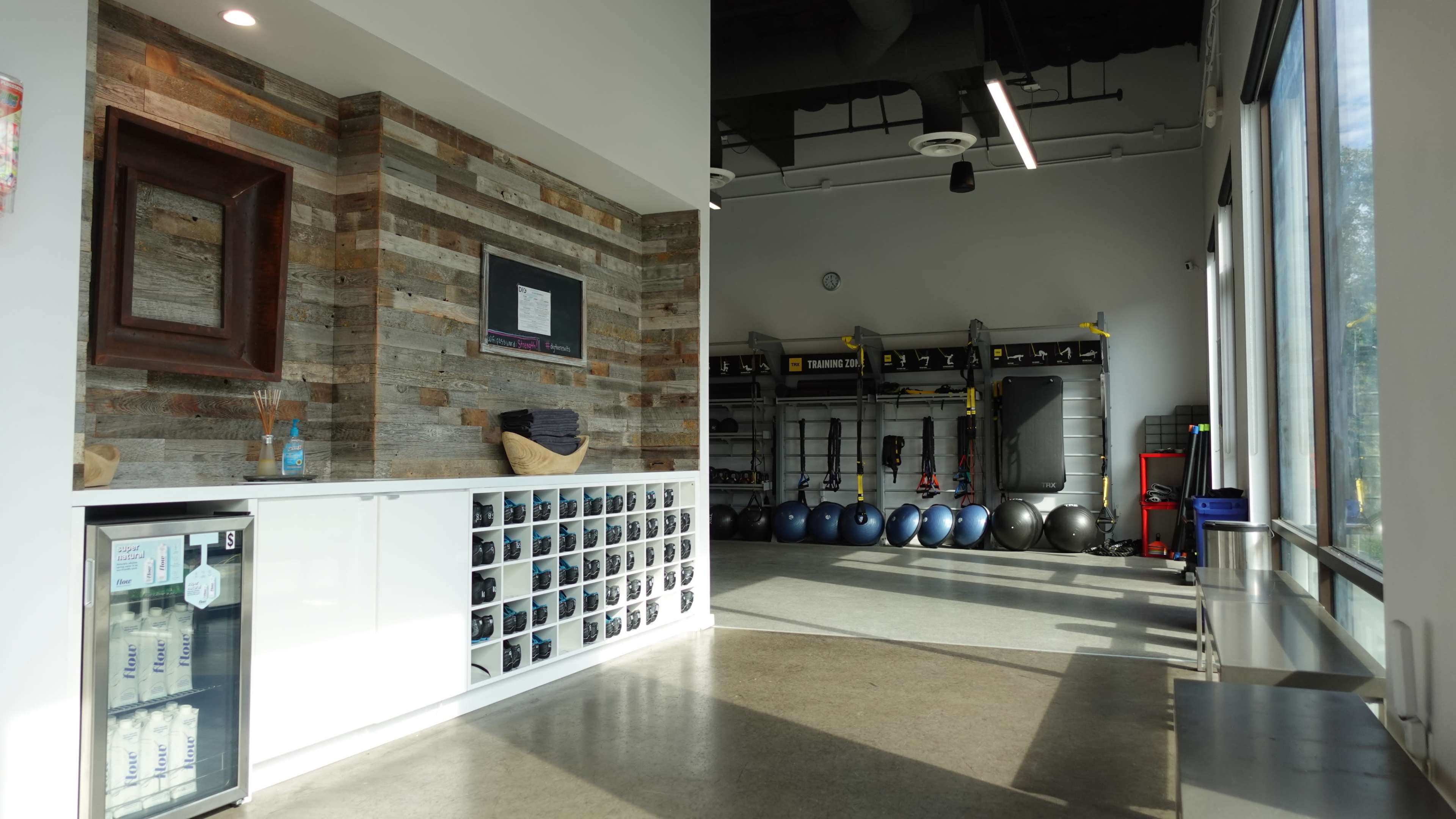 A modern gym interior with a reception area featuring a wall of cubby storage and a workout space equipped with exercise equipment and stability balls.