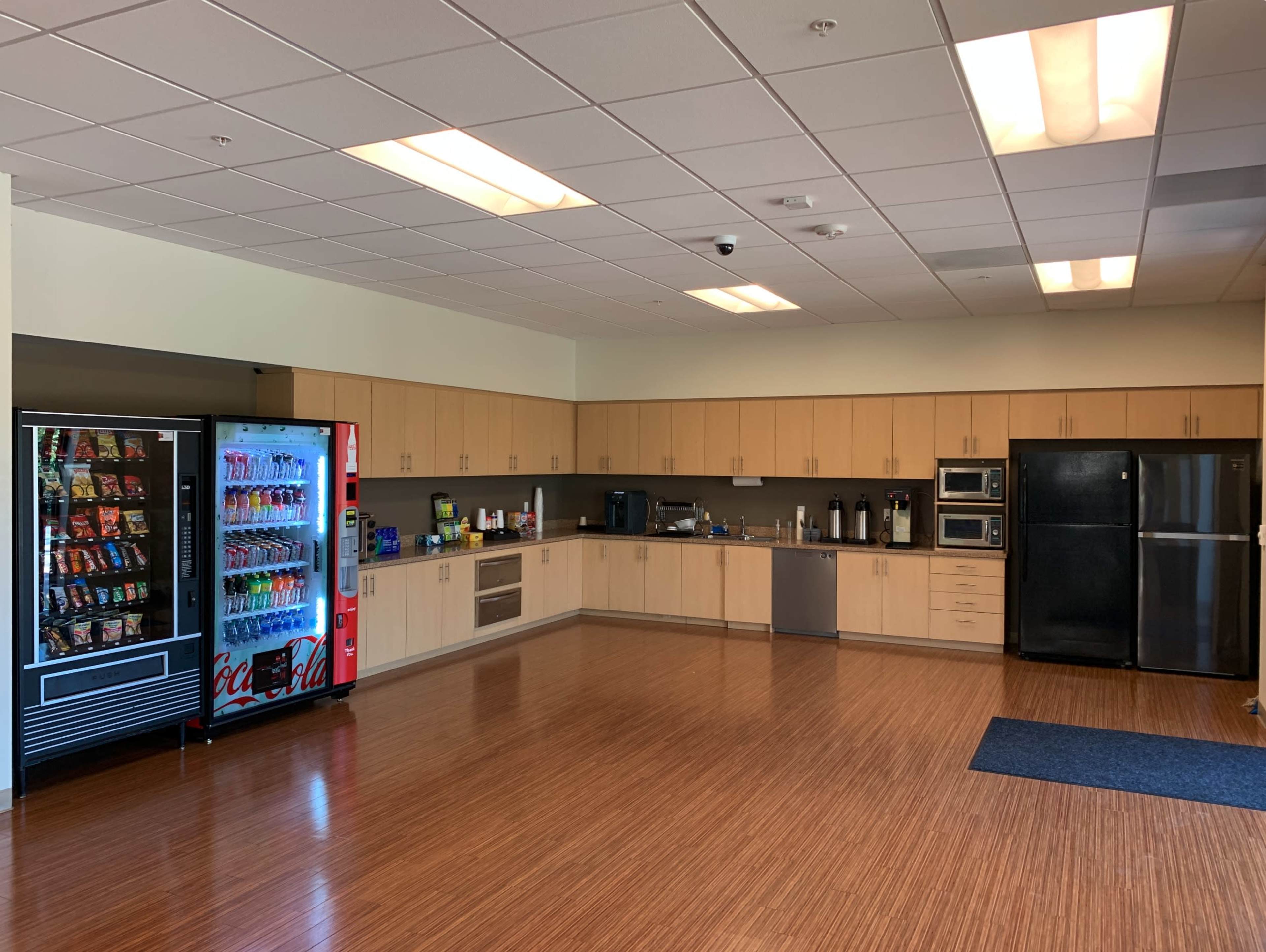 A kitchen area equipped with cabinets, a refrigerator, a microwave, and a beverage vending machine.