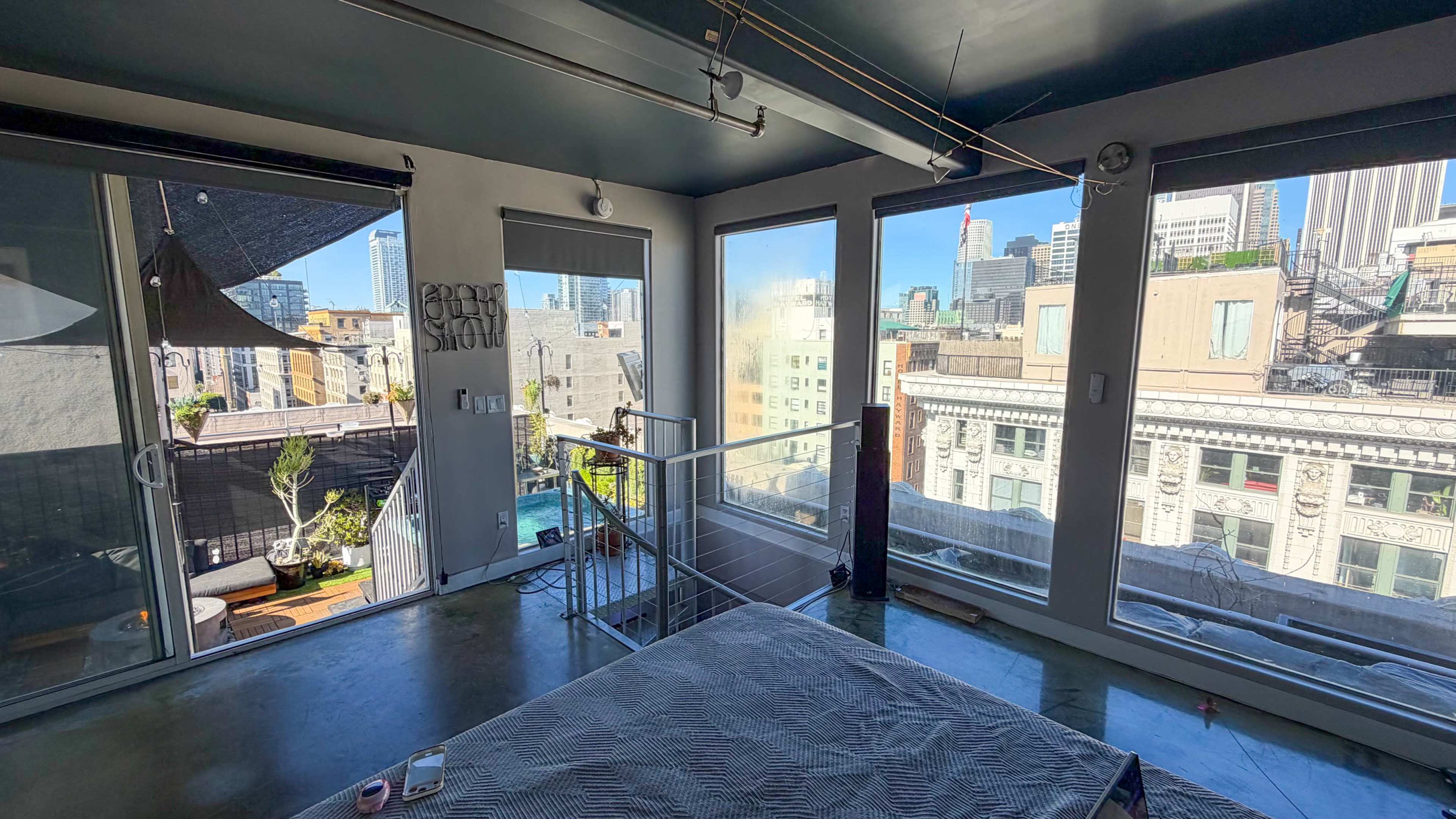 The image shows a modern bedroom with large windows that offer a view of a city skyline.