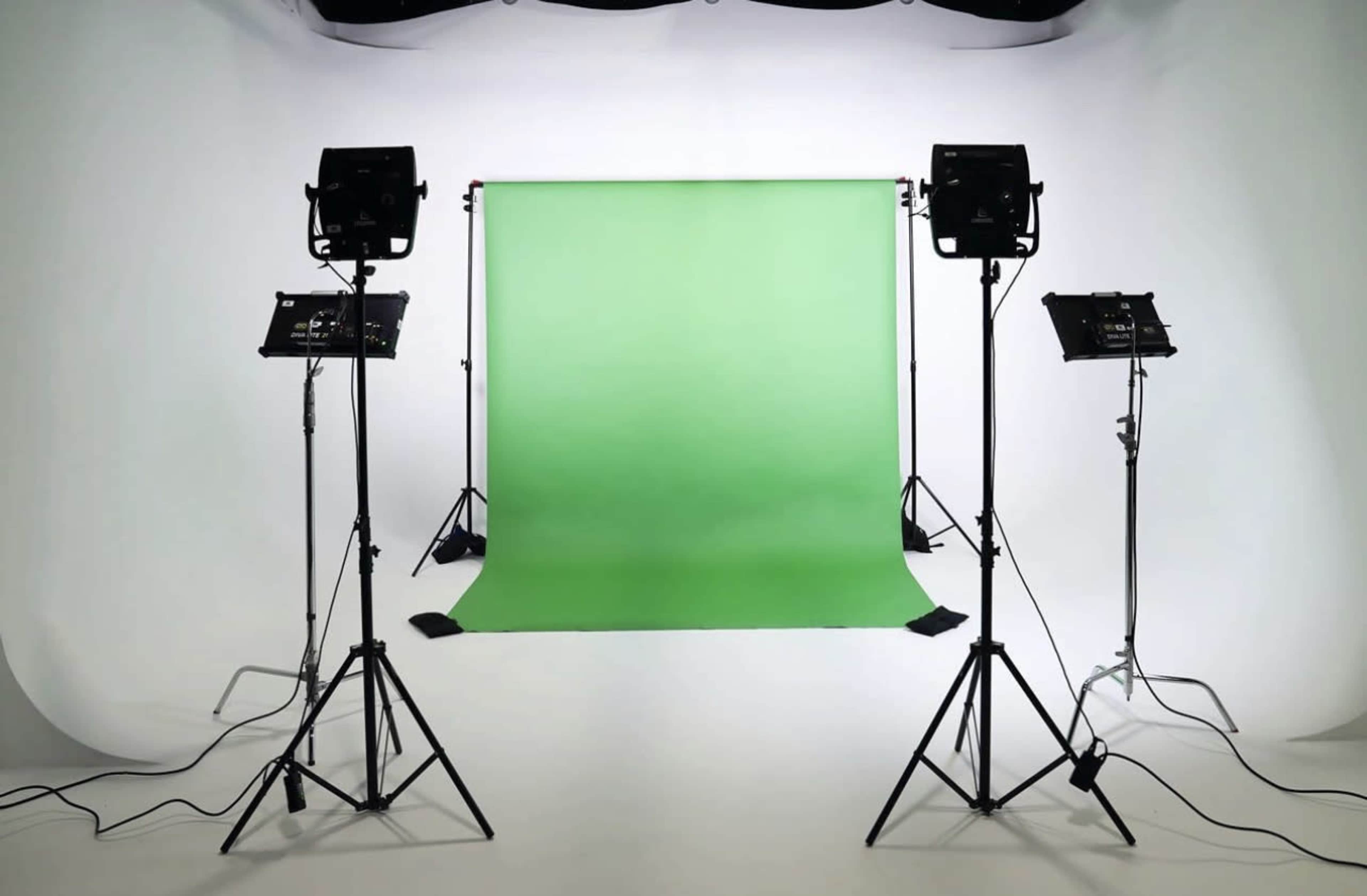 A photography studio features a green backdrop flanked by two lighting setups on tripods.