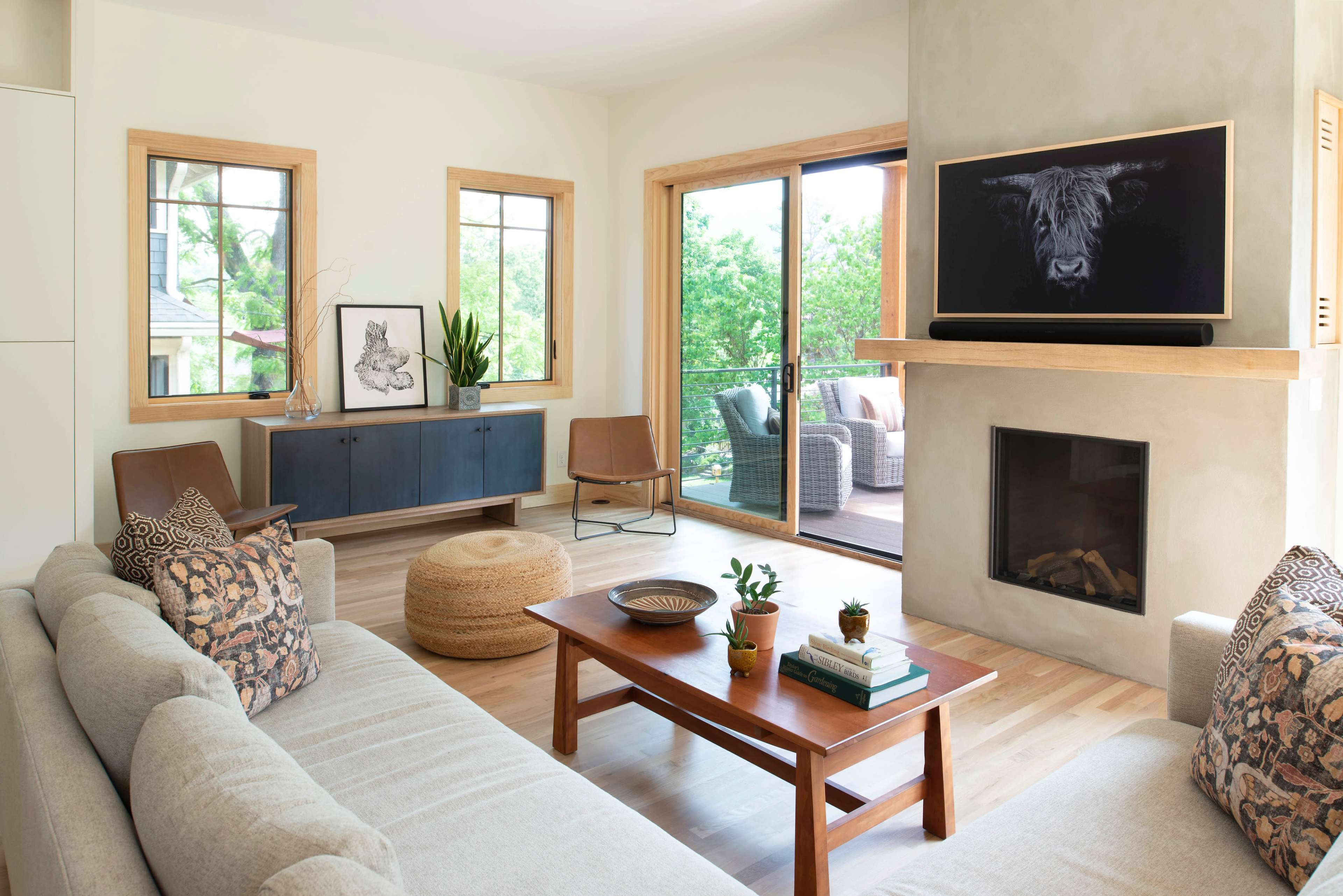 The living room features a light-colored sofa, a wooden coffee table, and large windows that overlook a green outdoor space.