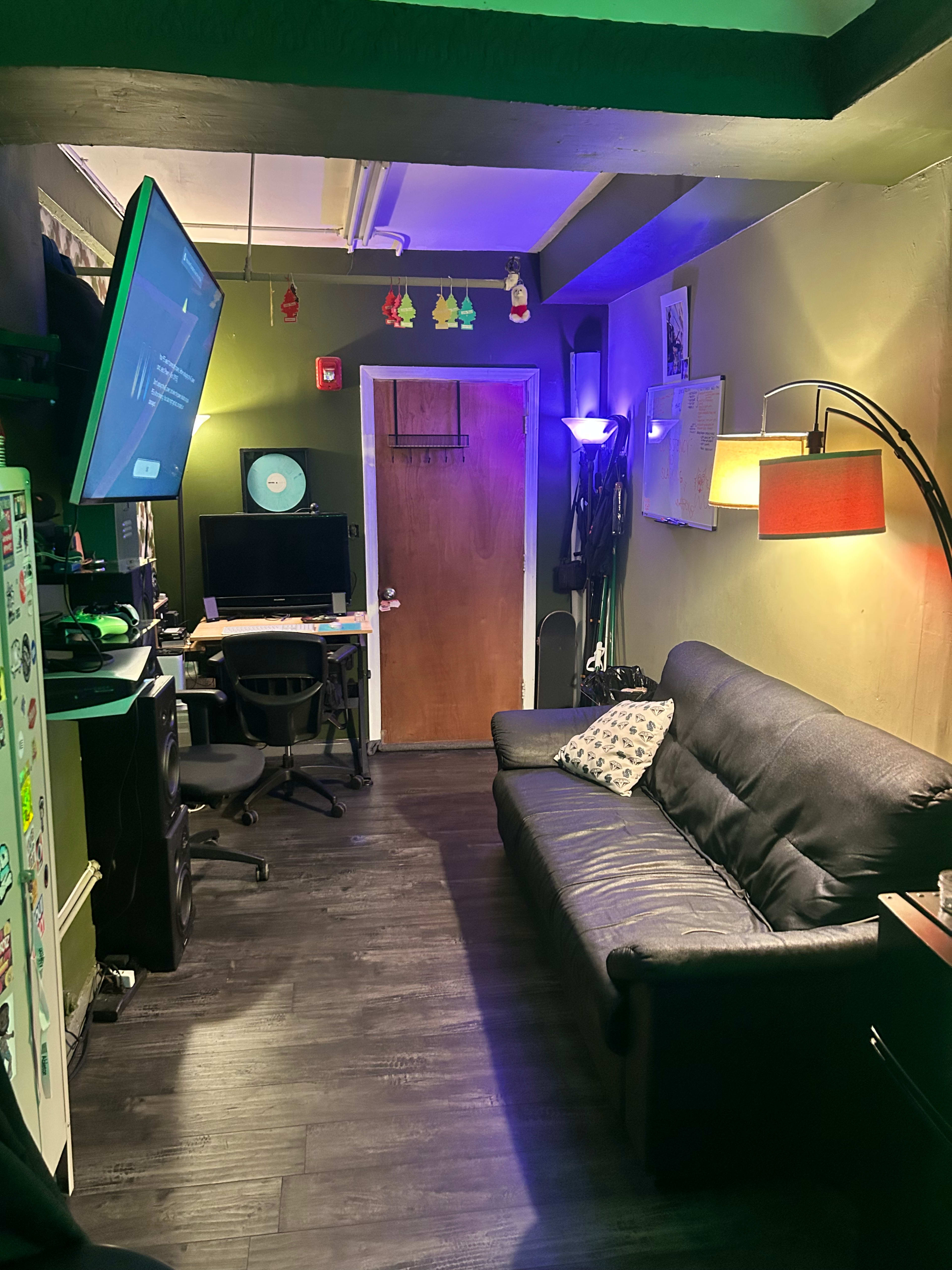 The image shows a small room with a black sofa, a computer setup on a desk, and colored lighting.