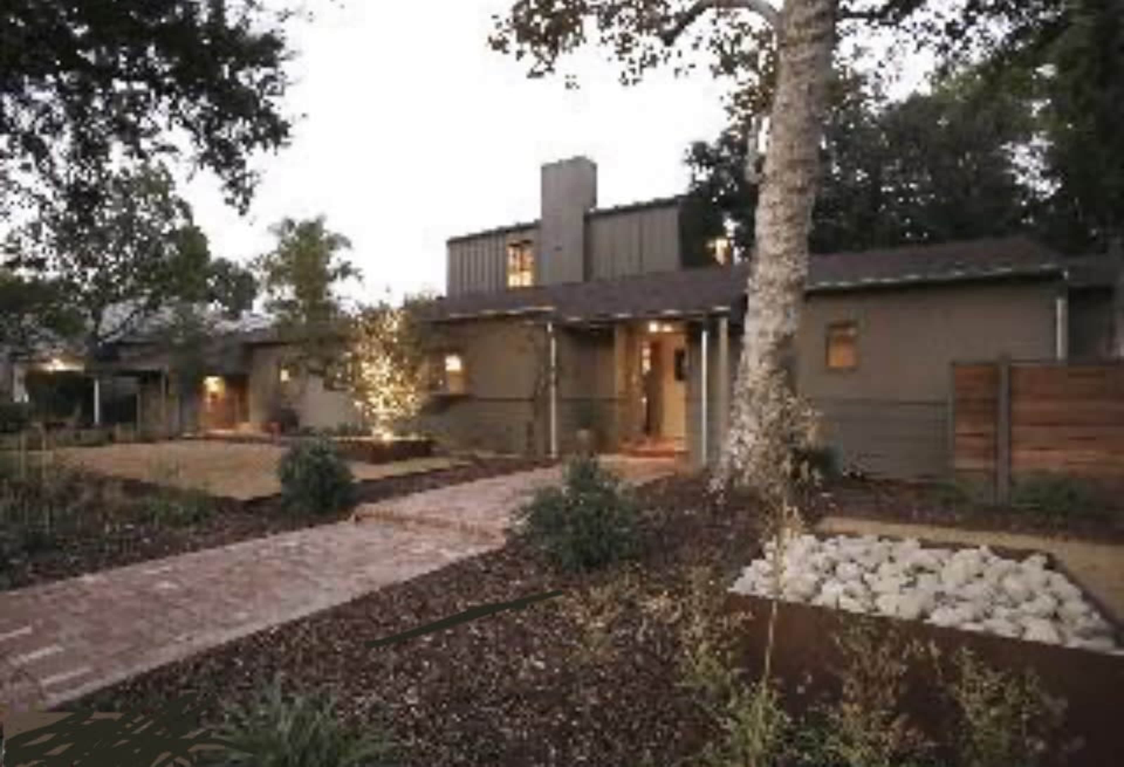 The image shows a modern house with a landscaped front yard, featuring a brick pathway leading to the entrance.