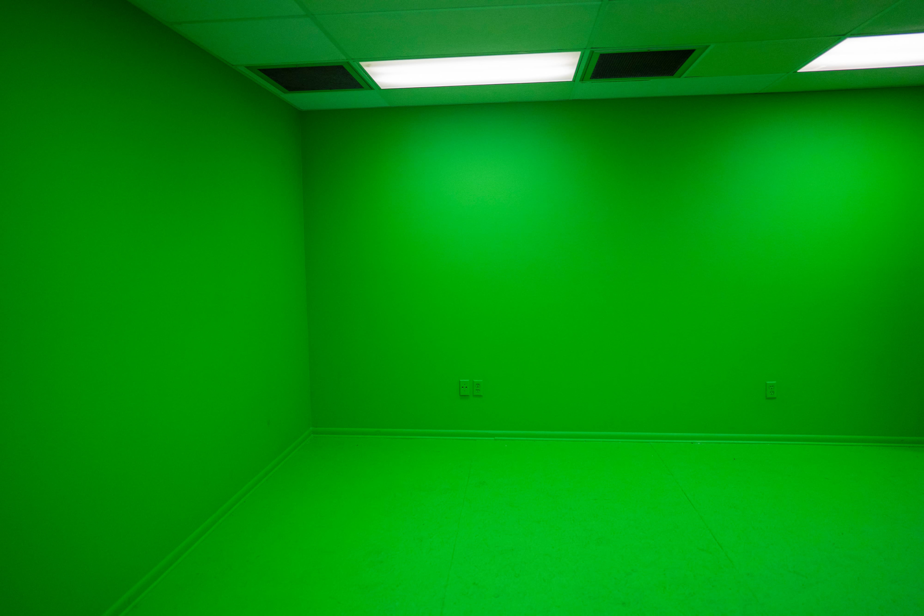 The image shows a room with all walls and the floor painted bright green, illuminated by fluorescent lights.