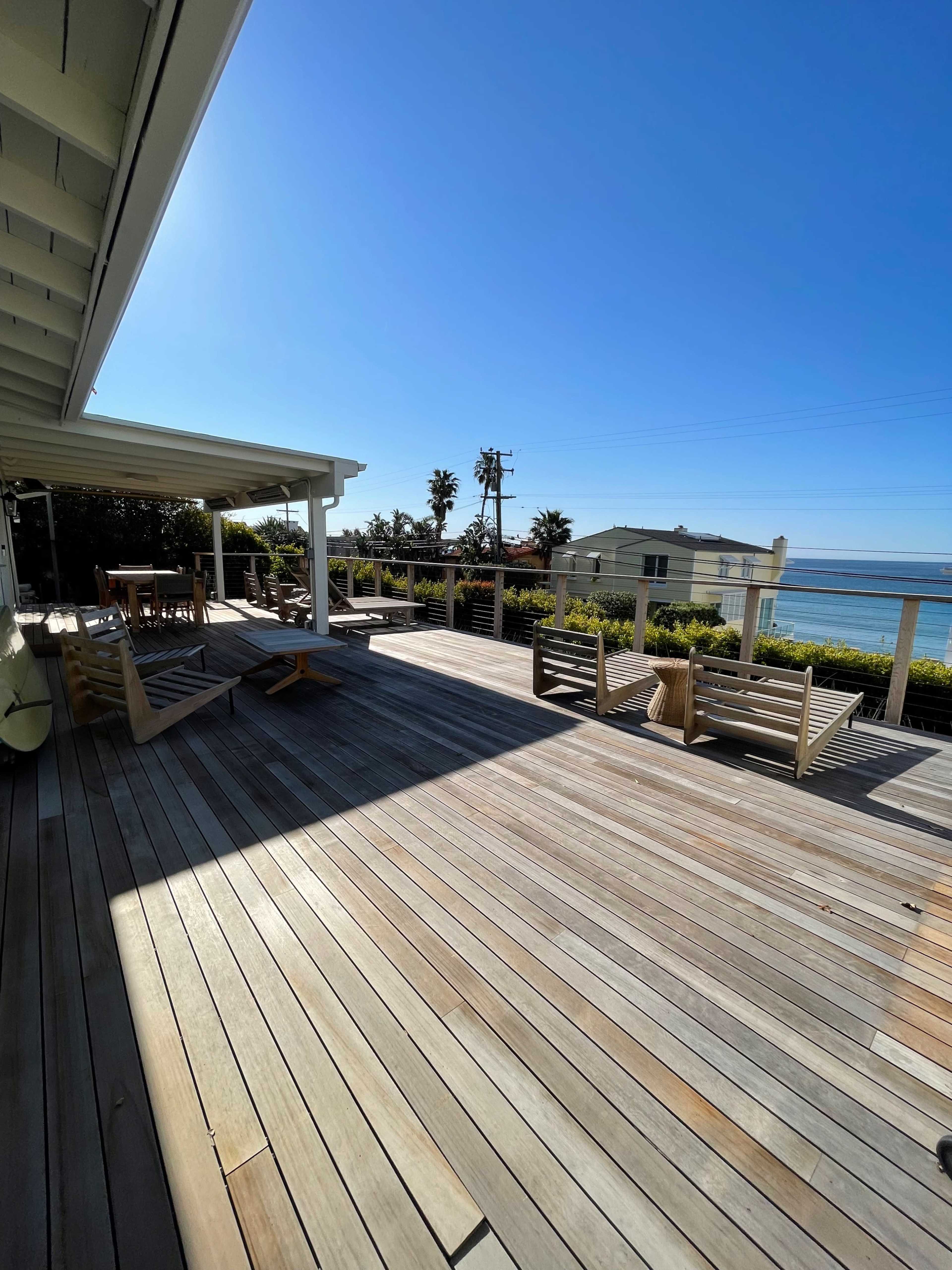 A wooden deck with several lounge chairs overlooks the ocean under a clear blue sky.