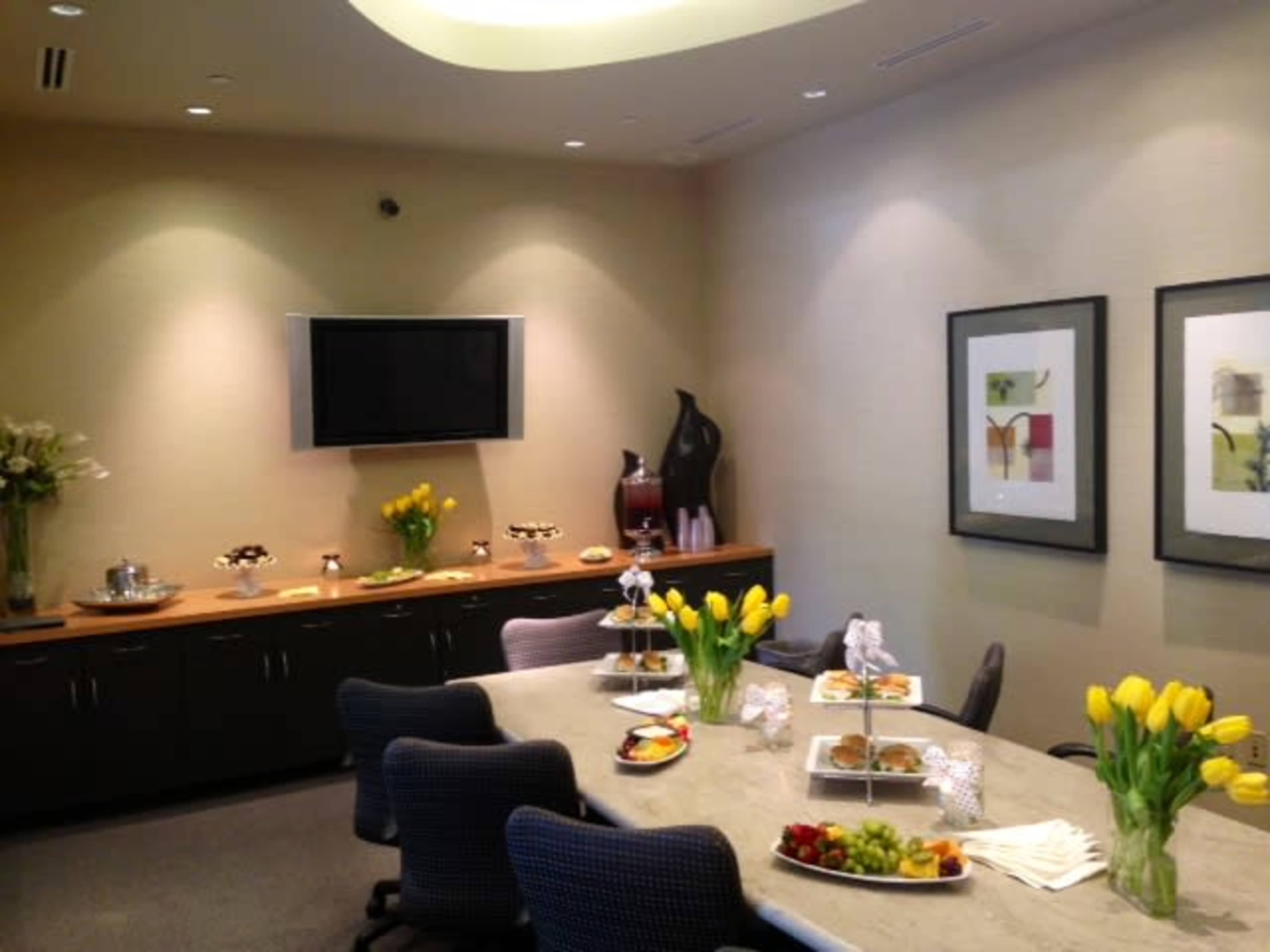 A conference room features a long table set with various food platters and a television mounted on the wall.