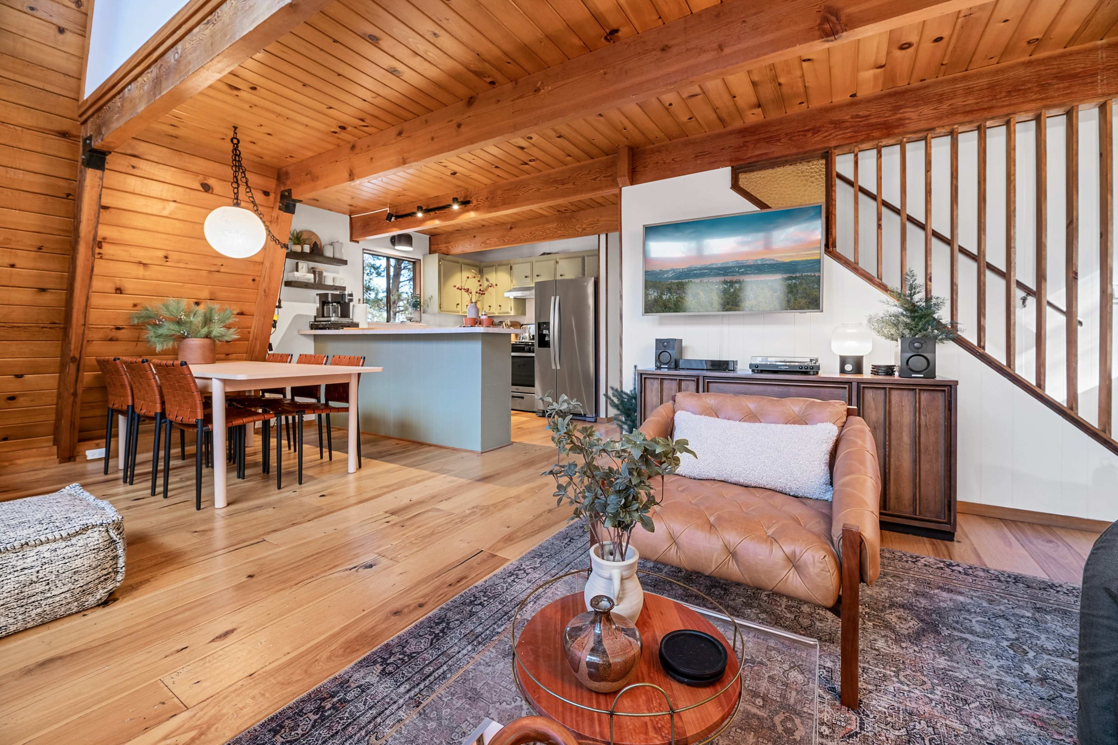 A wooden interior living space featuring a dining area, kitchen, and lounge with a leather sofa and a coffee table.