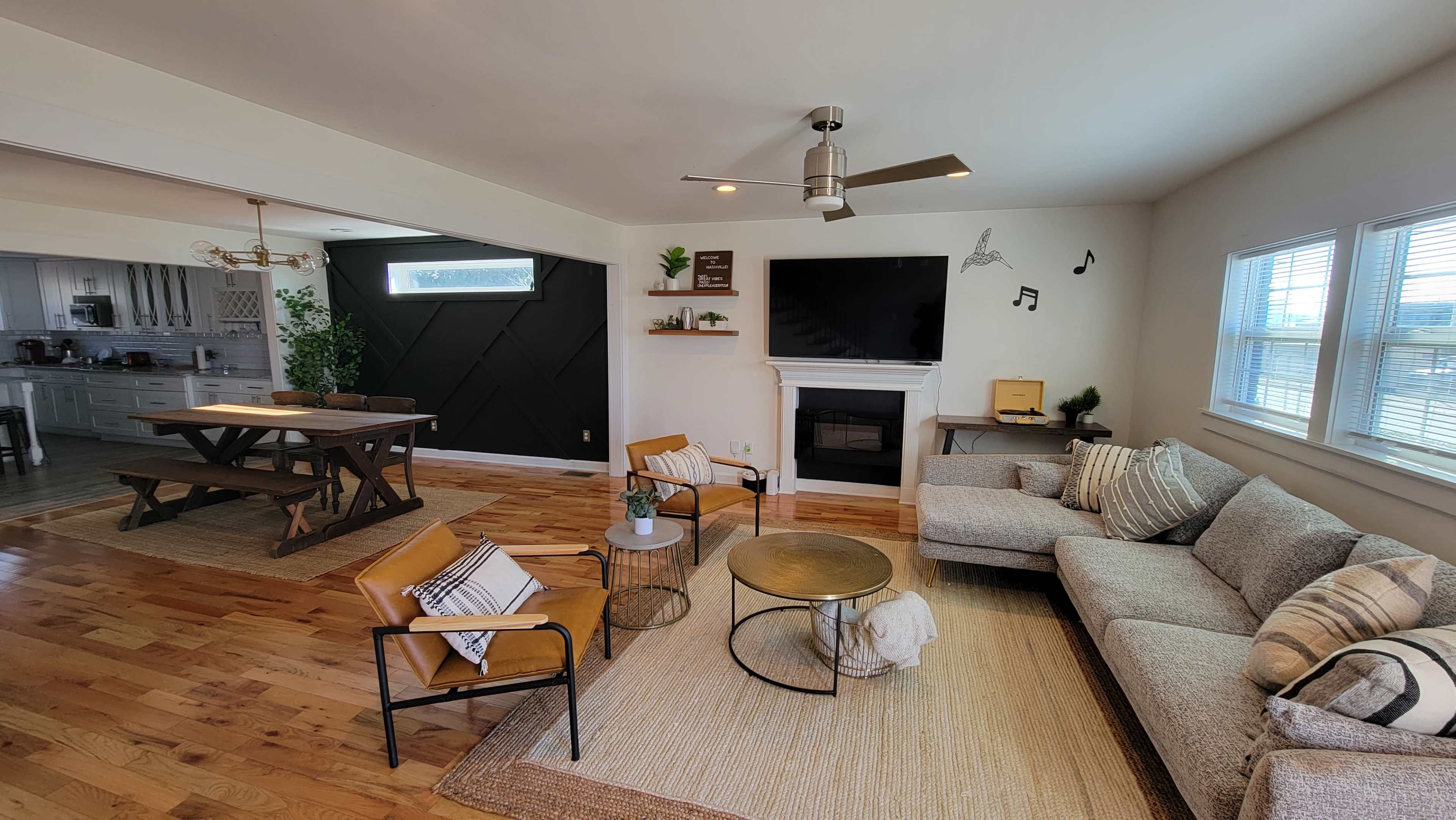 A modern living room featuring a gray sectional sofa, a circular coffee table, and a dining area with a wooden table and chairs, complemented by a wall-mounted TV and decorative elements.