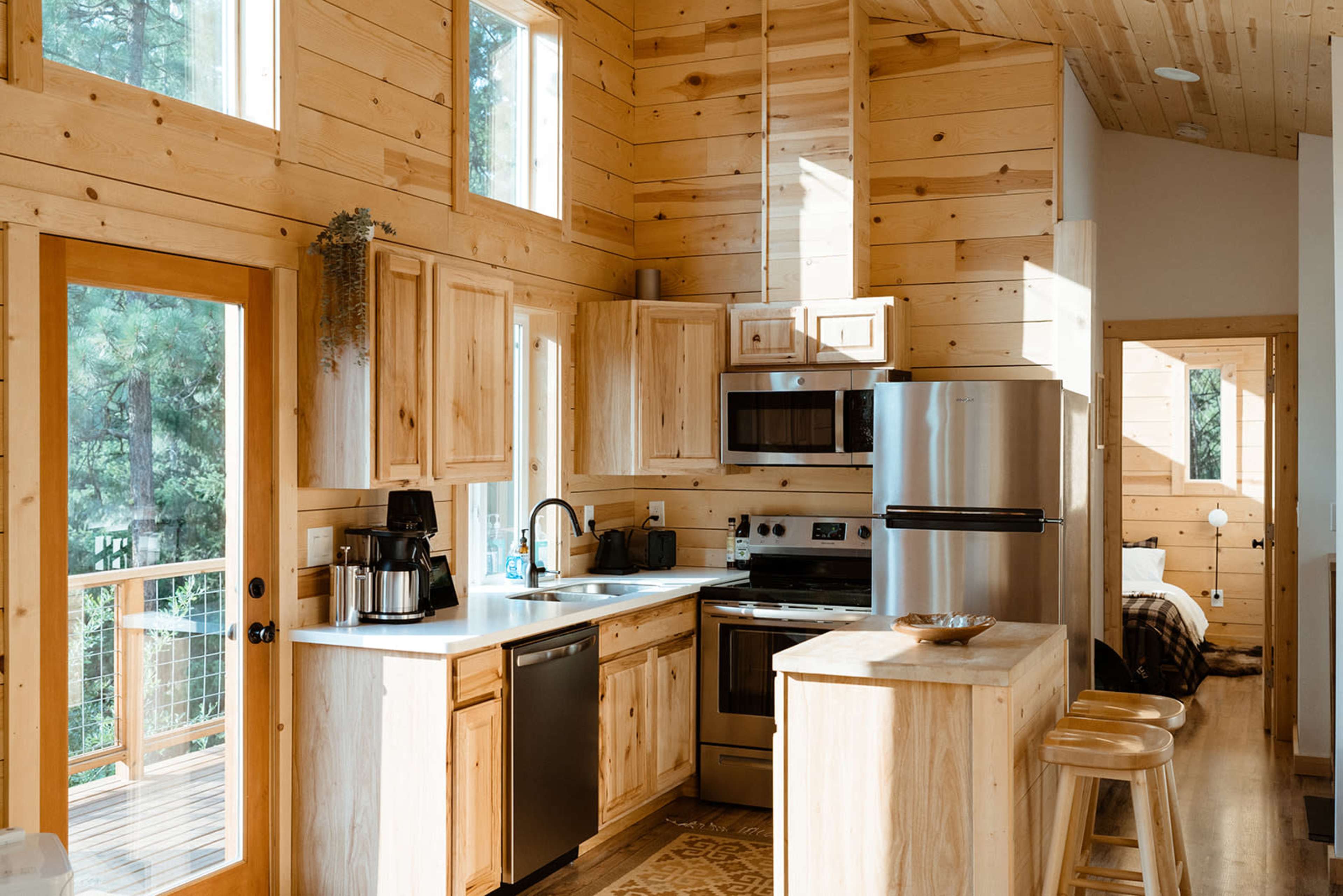 The image shows a modern kitchen with wooden walls, stainless steel appliances, and a countertop island with bar stools.