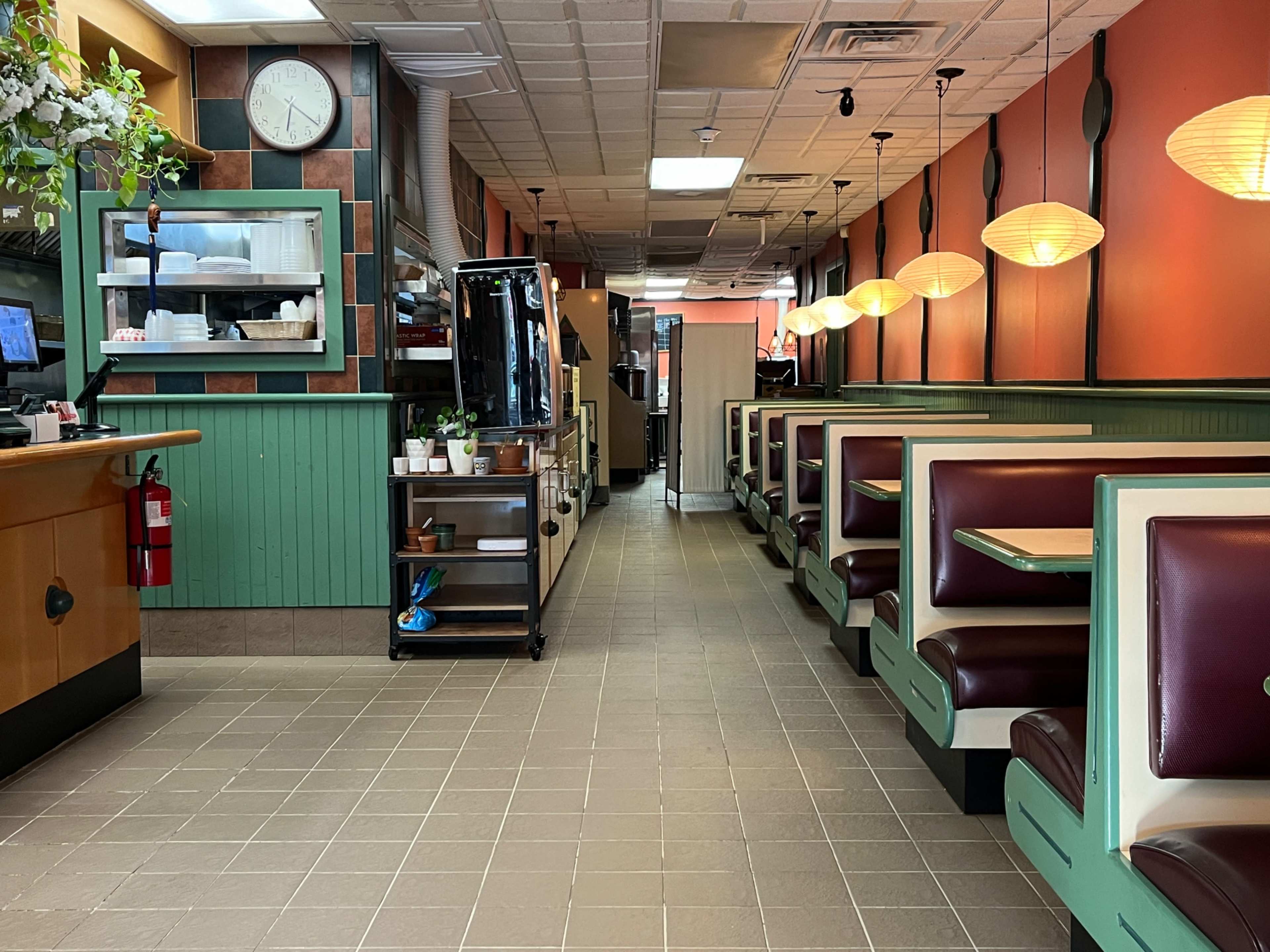 The interior of a diner with green and orange walls, booth seating on one side, and a serving counter on the left.