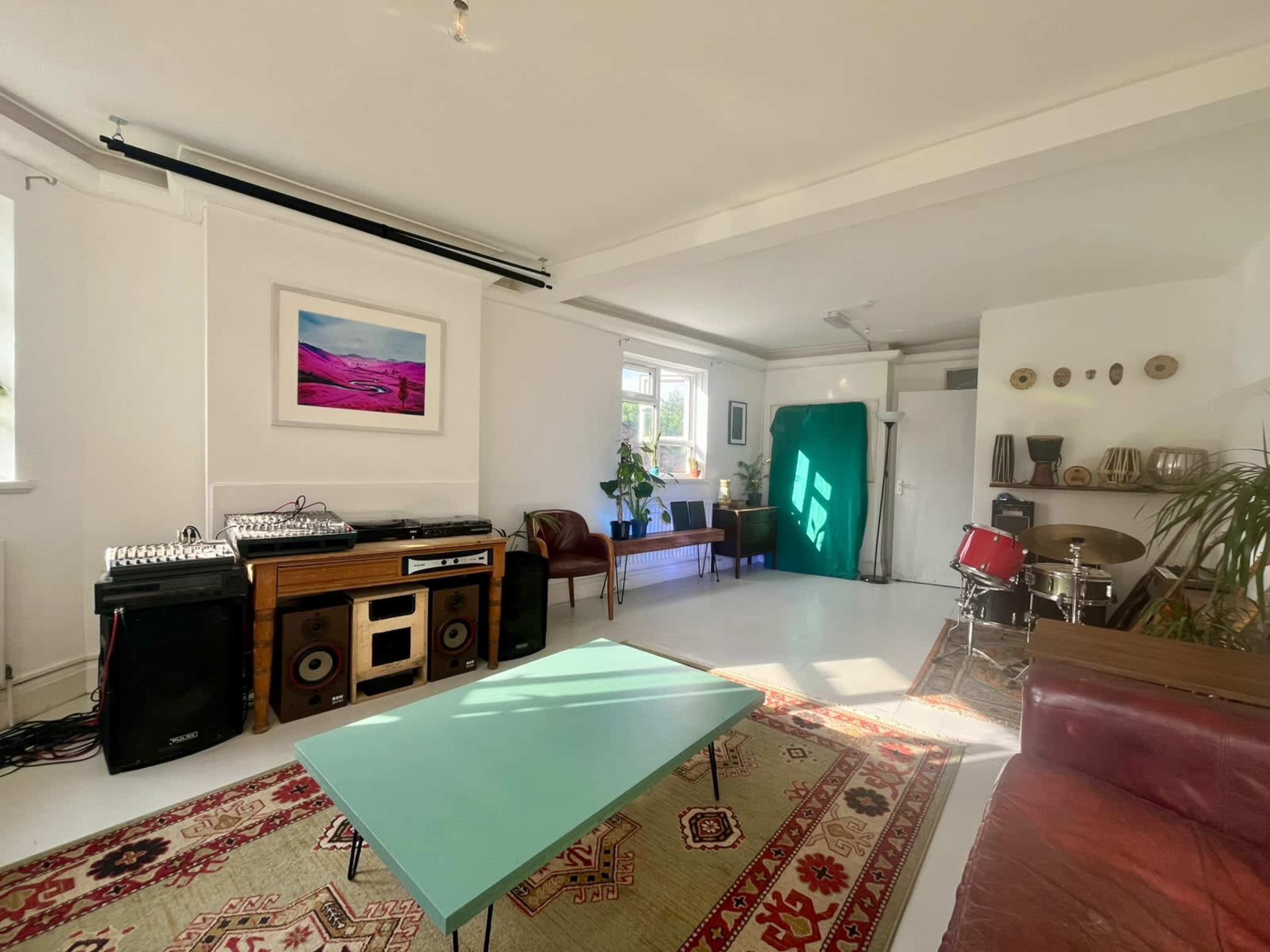The scene features a modern living space with a green backdrop, musical equipment, a wooden console, a couch, and a coffee table on an area rug.