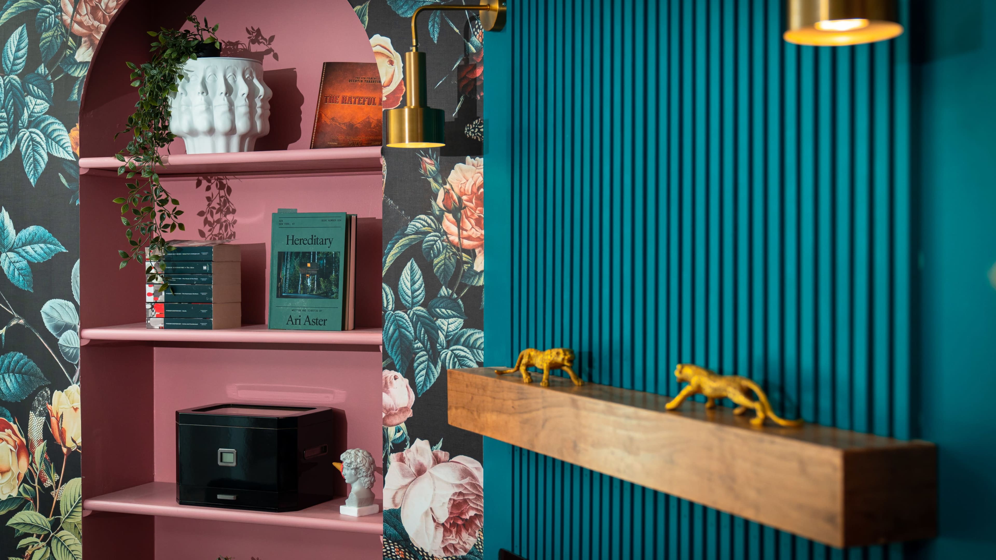 The image features a colorful interior scene with a shelf displaying books, decorative objects, and a floral wallpaper backdrop.