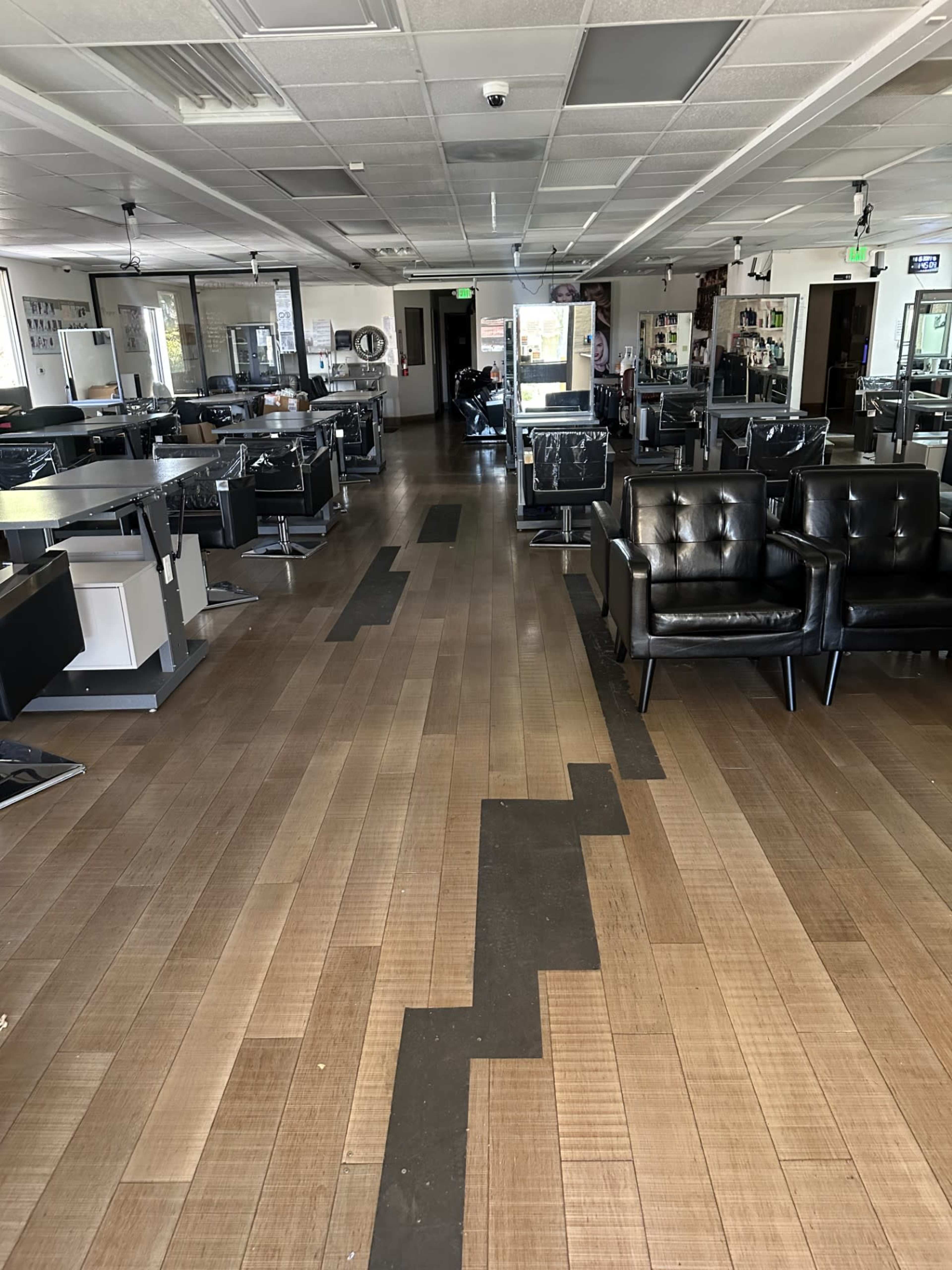The interior of a sparsely furnished salon with black chairs and wooden flooring.