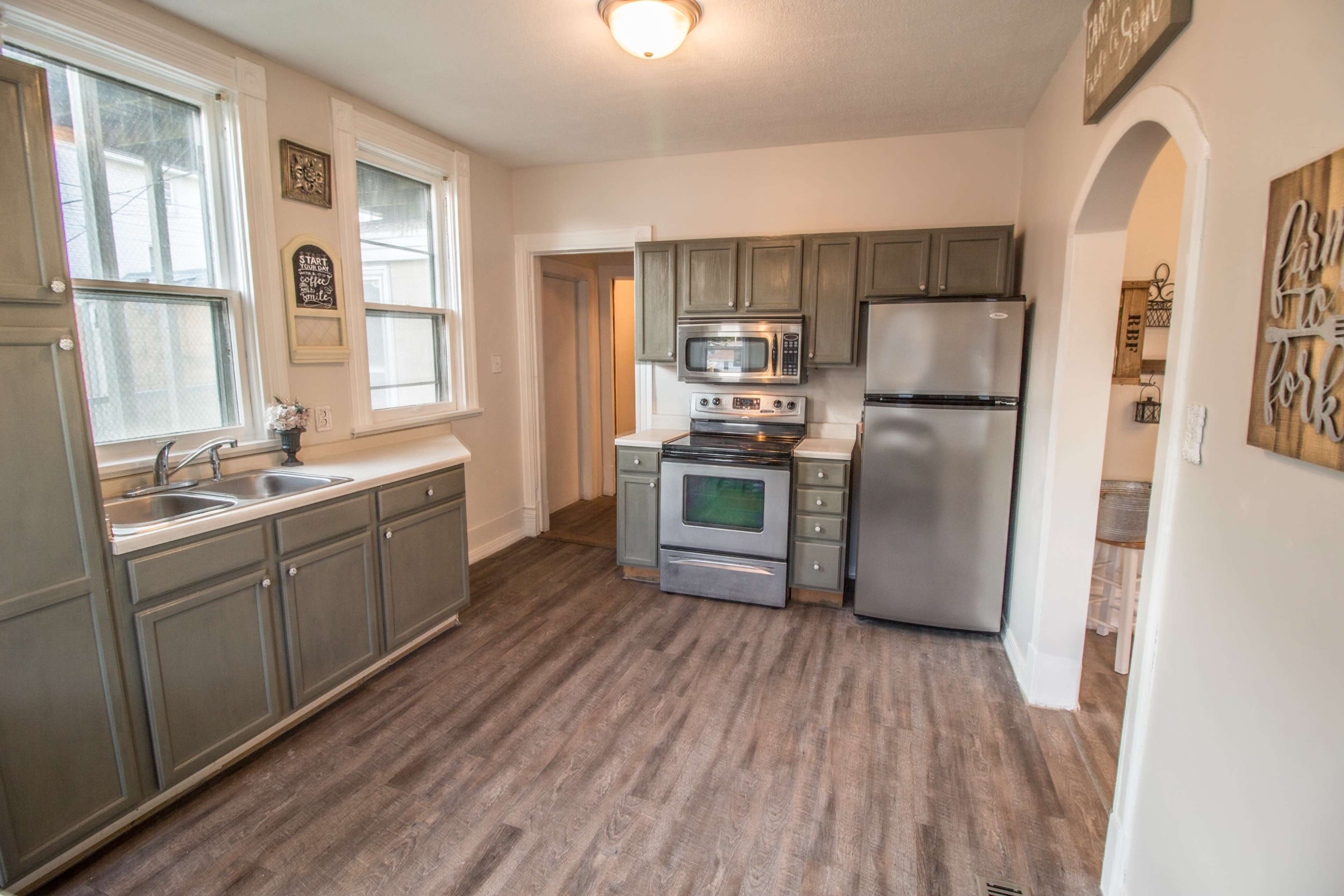 A kitchen with gray cabinets, stainless steel appliances, and a wooden floor.