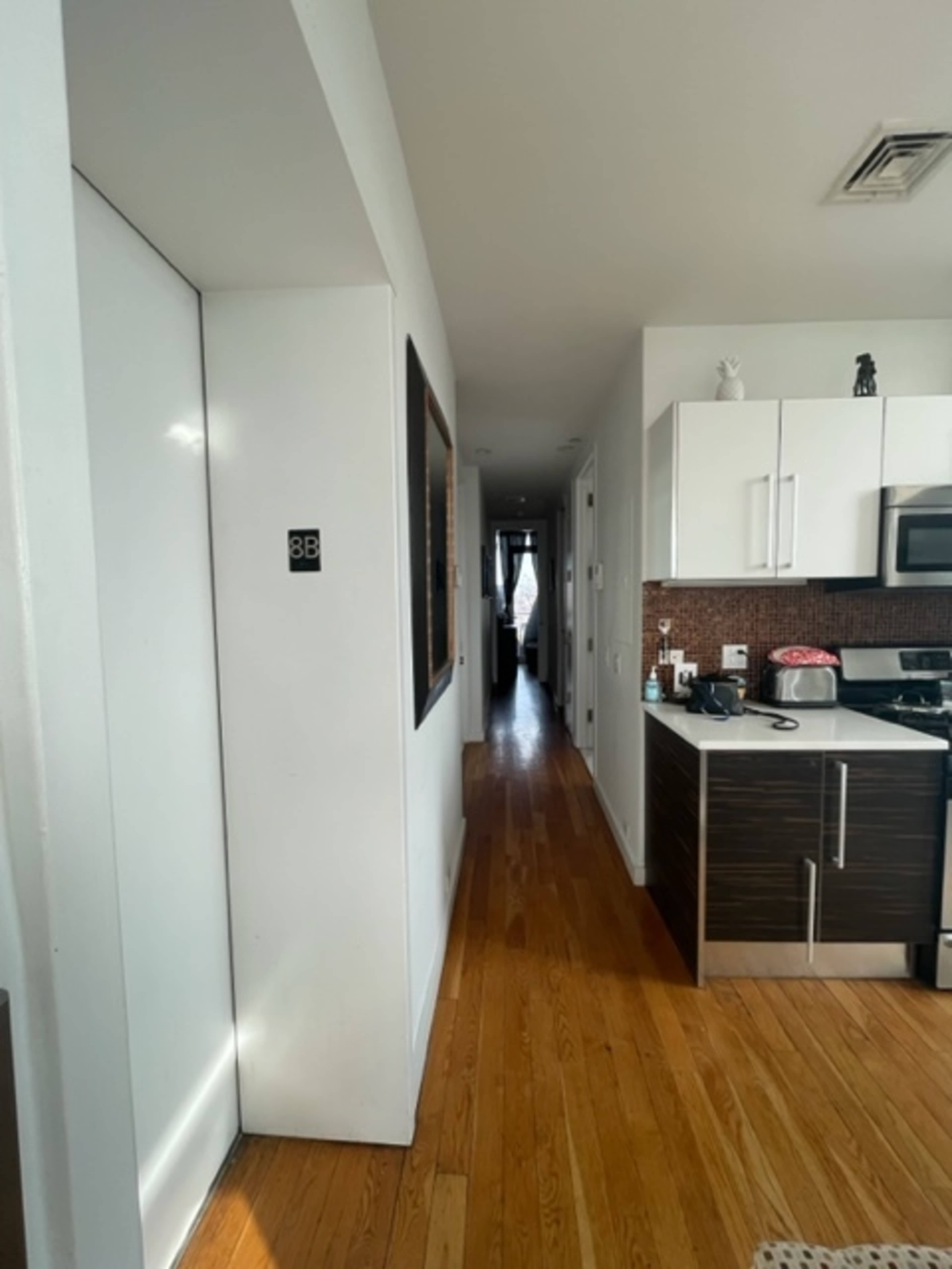 The image shows a hallway leading to a kitchen on the right, with a door marked "3B" and a mirror at the far end.