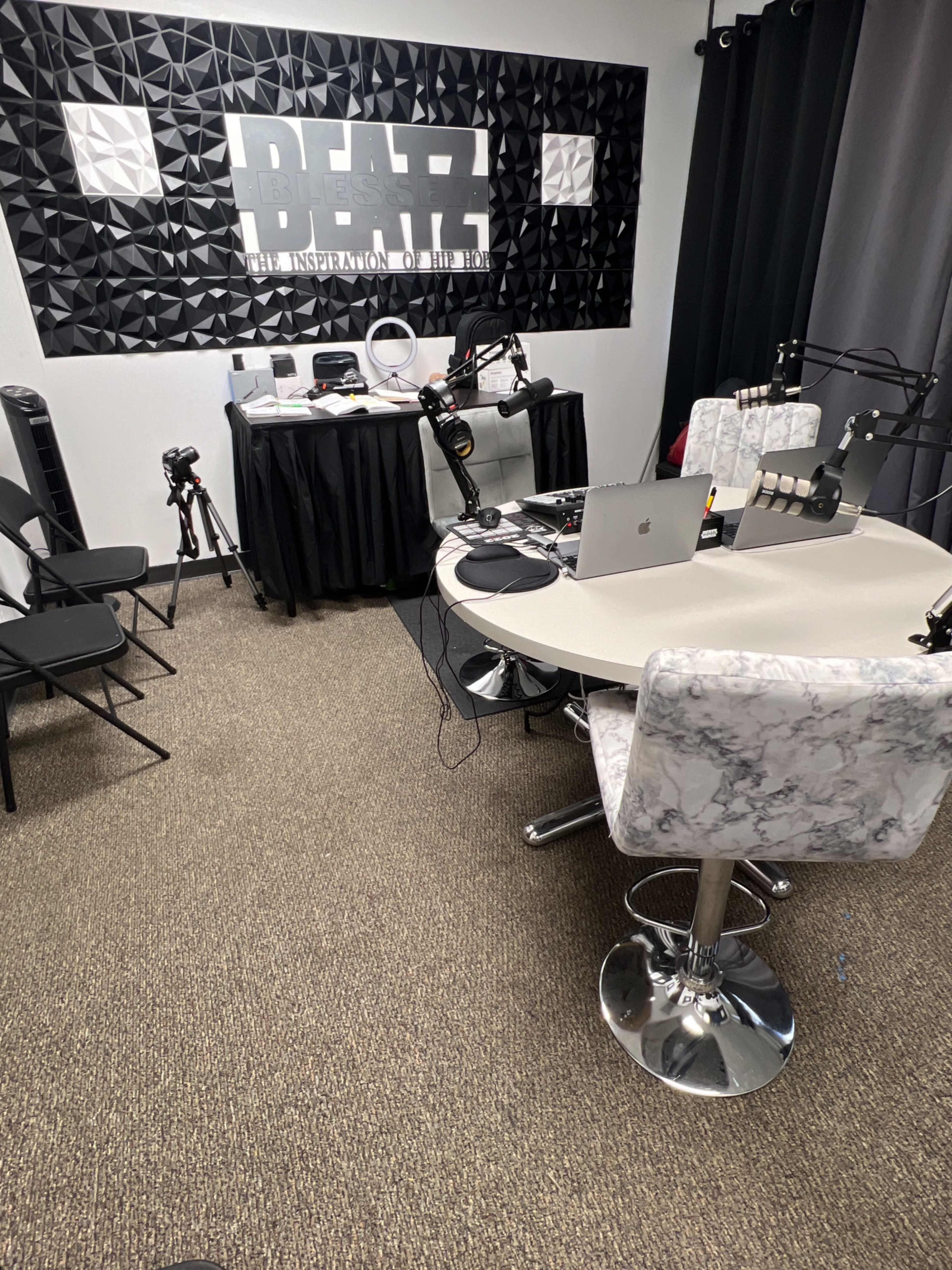The image shows a recording studio setup with a round table, microphones, and equipment against a textured wall featuring the word "BEATZ."