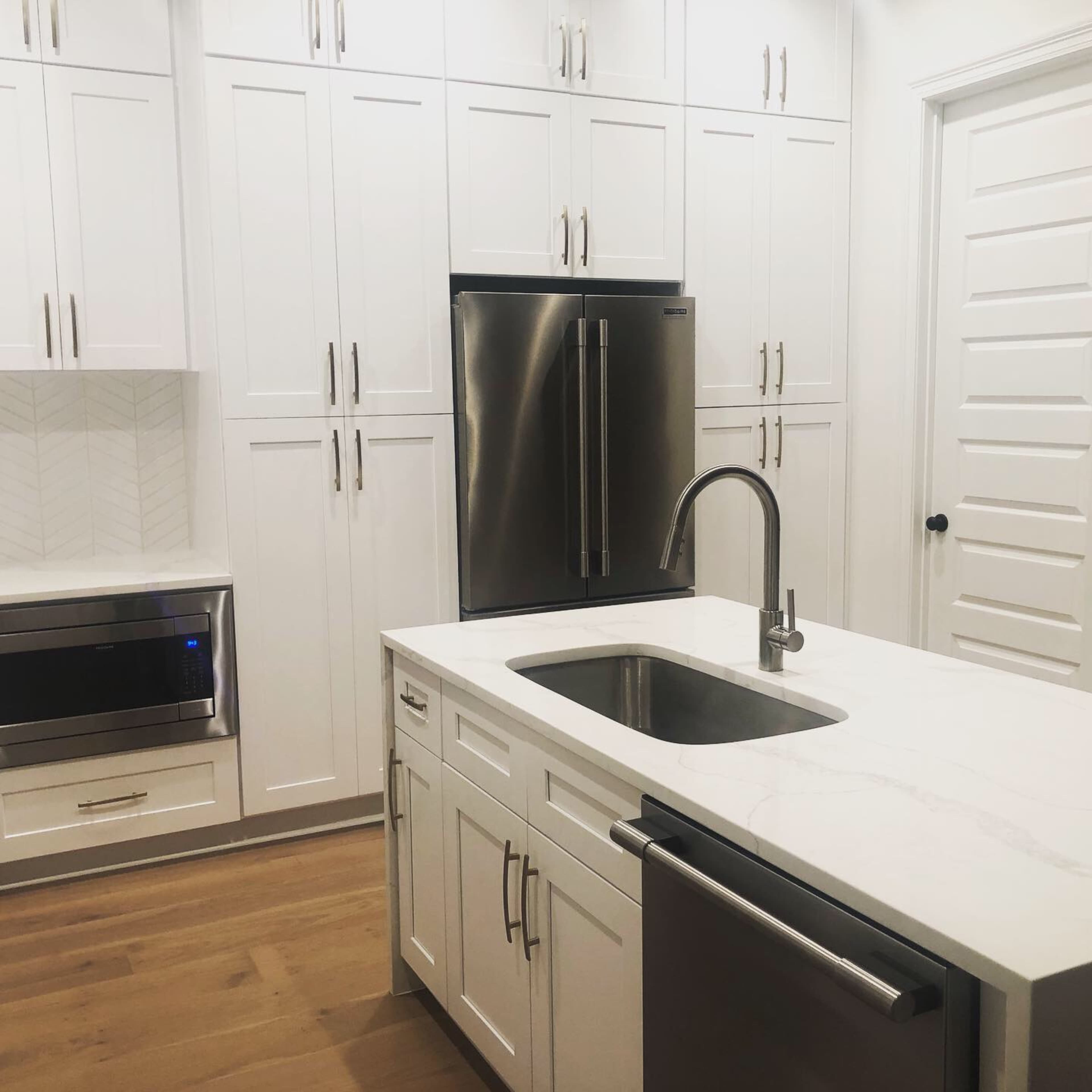 A modern kitchen with white cabinetry, stainless steel appliances, a sink integrated into the island, and light hardwood flooring.