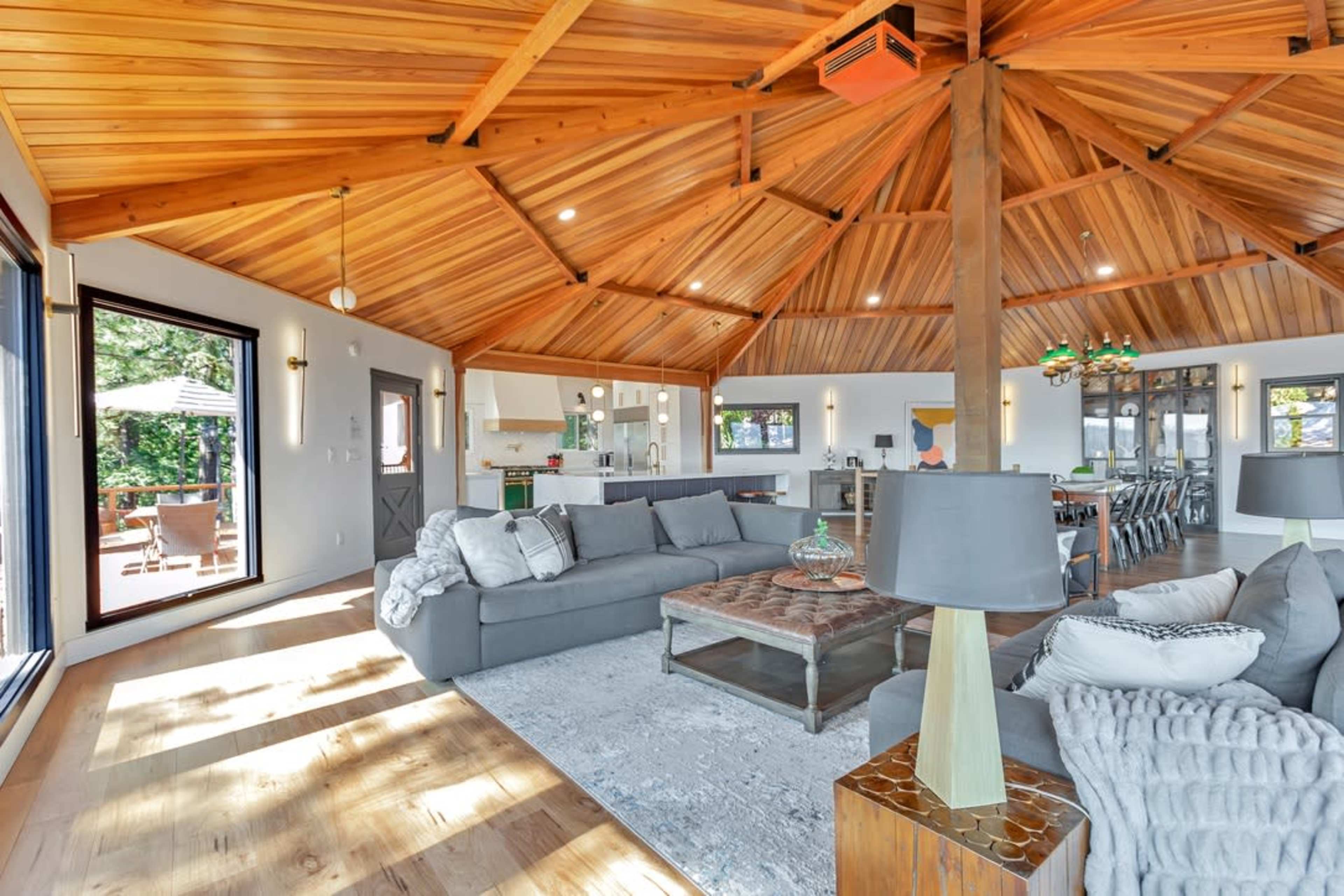 A spacious living area features a circular wooden ceiling, comfortable seating, and large windows that open to an outdoor space.