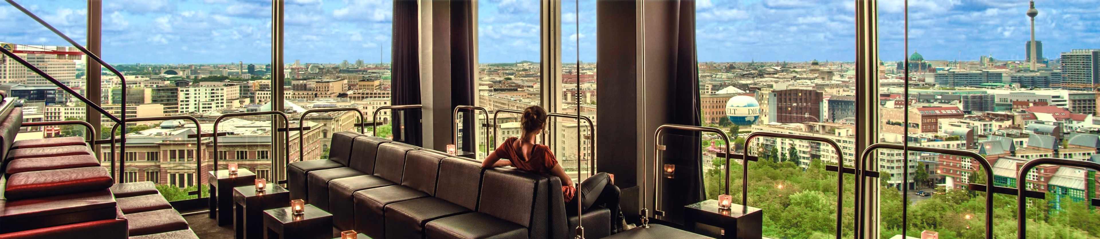 A person sits on a long bench in a high-rise lounge with large windows overlooking a cityscape.