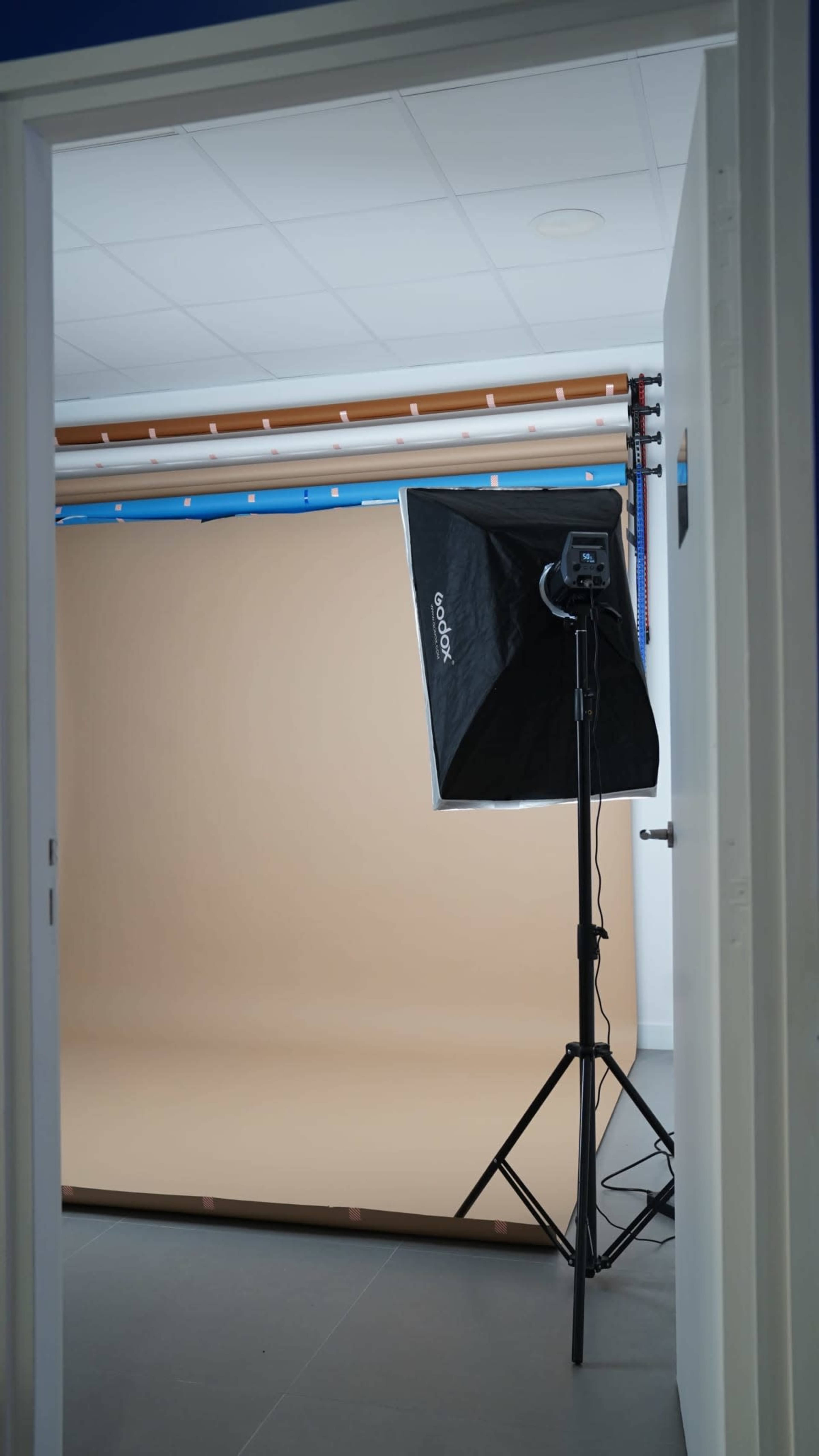 A photography studio is visible through an open door, featuring a softbox light and a seamless backdrop.