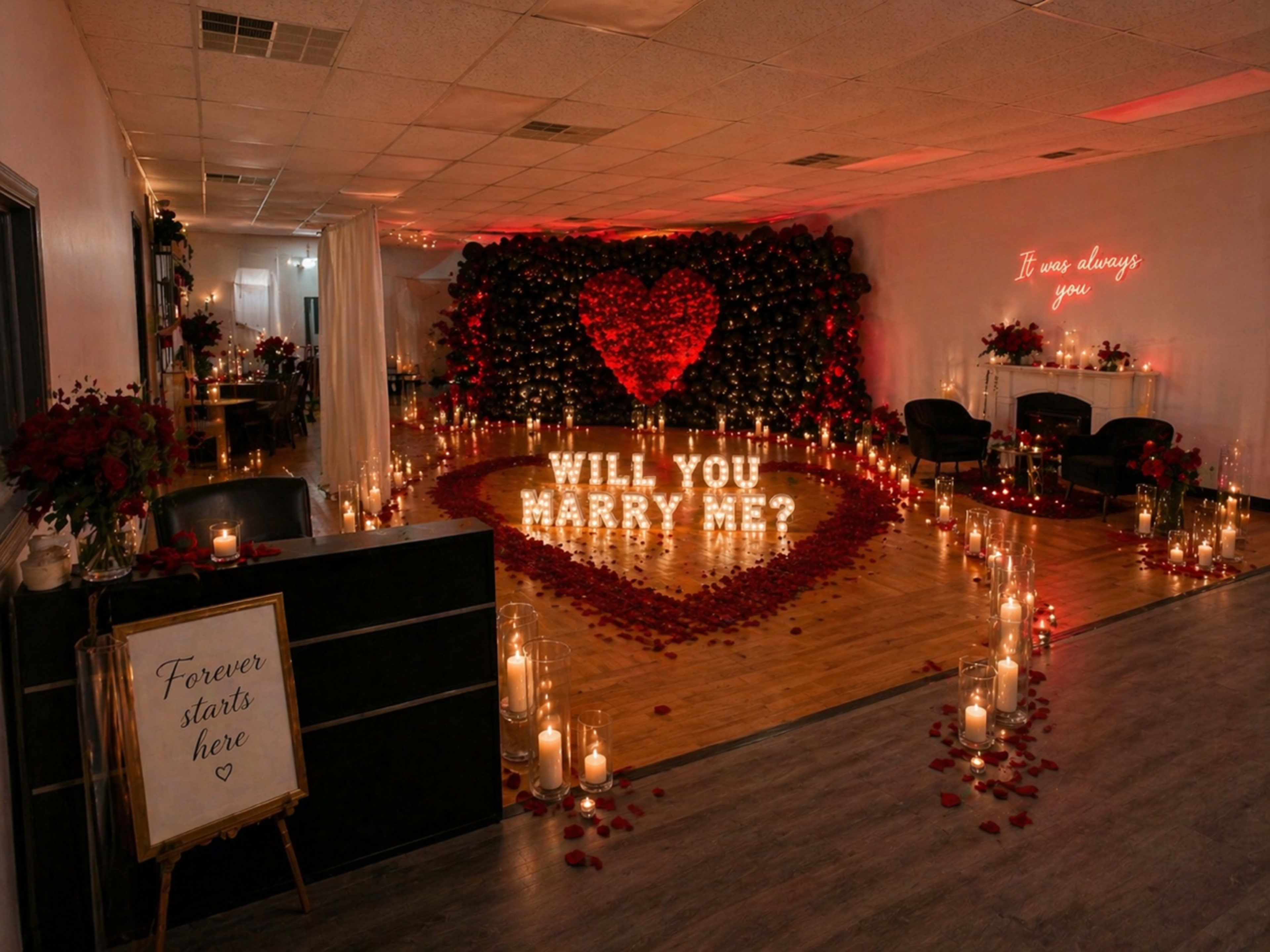The image shows an elegantly decorated room with a large heart made of roses and a proposal sign that reads "WILL YOU MARRY ME?" surrounded by candles and petals.