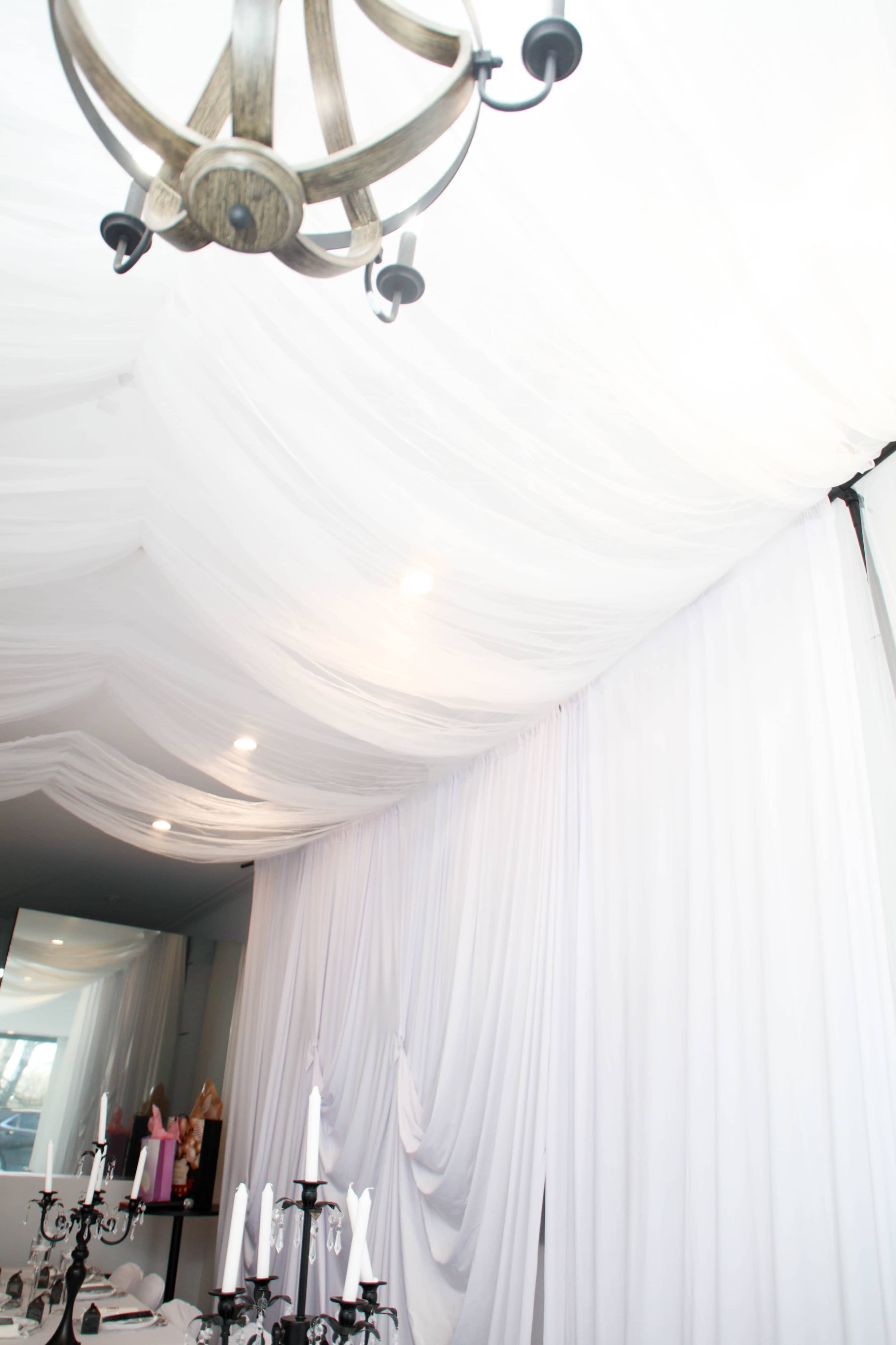 The image shows a ceiling draped in white fabric, with a chandelier and soft lighting illuminating the space.