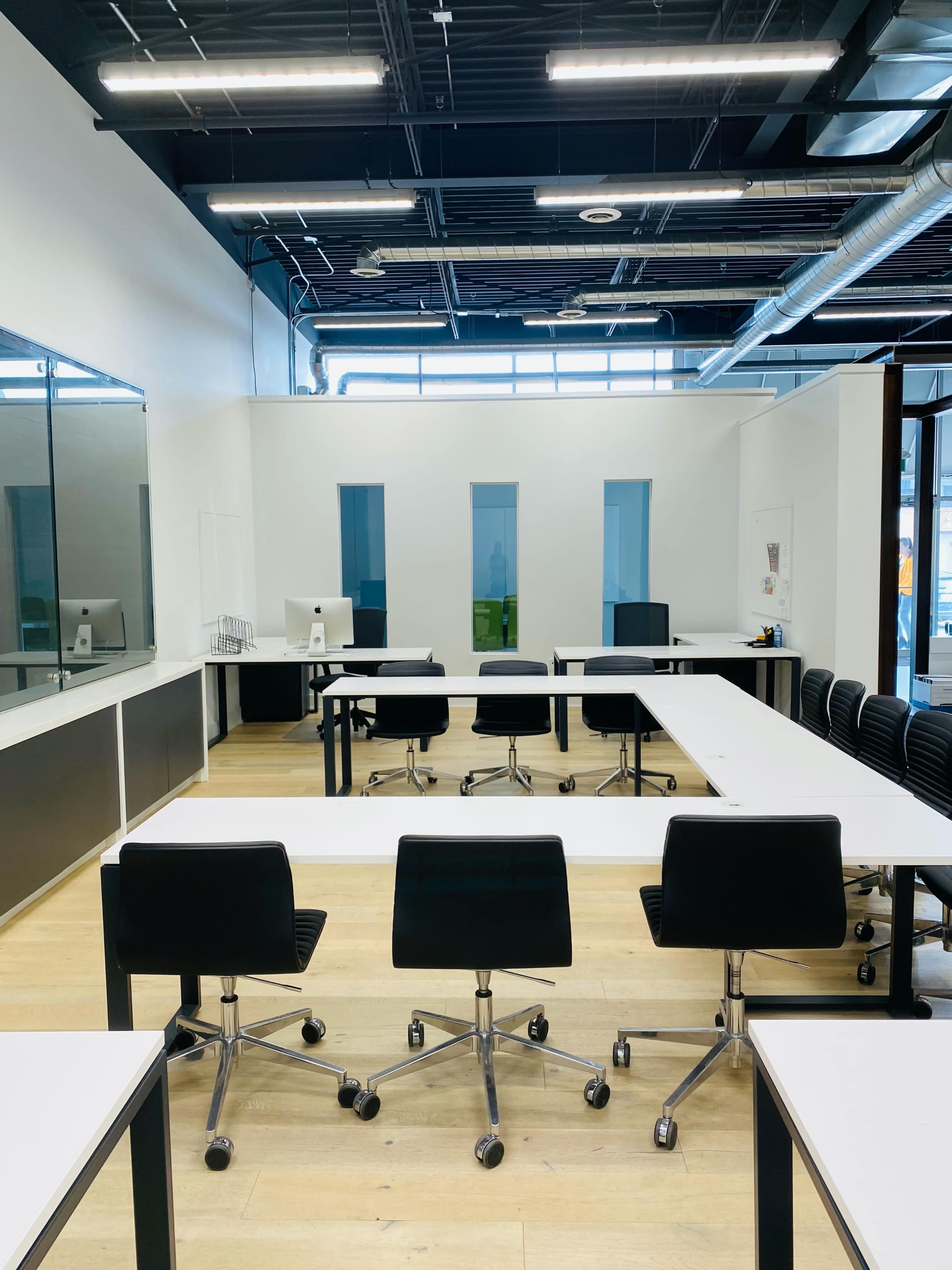 A modern office space with several tables arranged for collaborative work and black rolling chairs.
