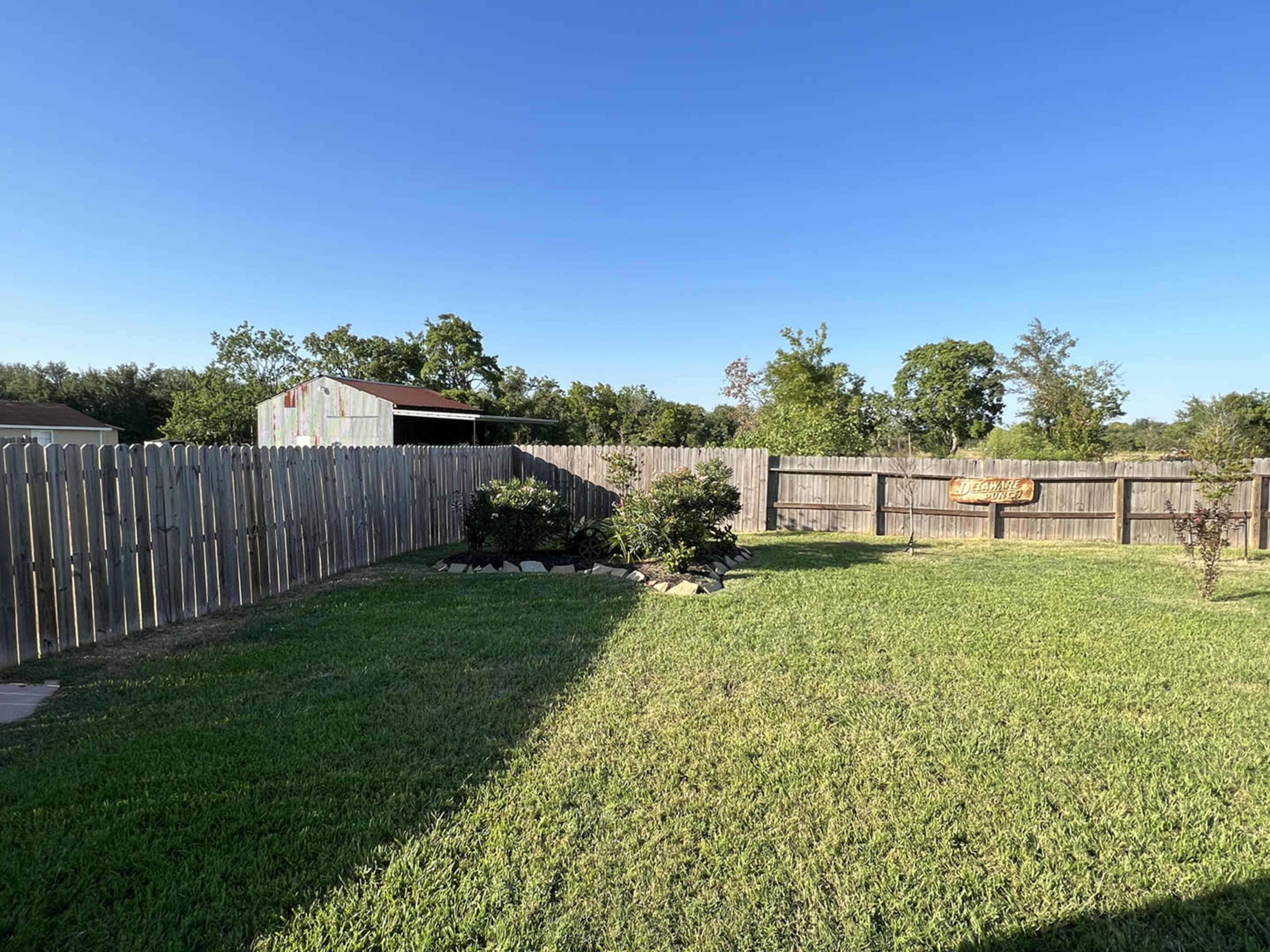 A well-maintained backyard with a wooden fence, green grass, and a shed in the background.