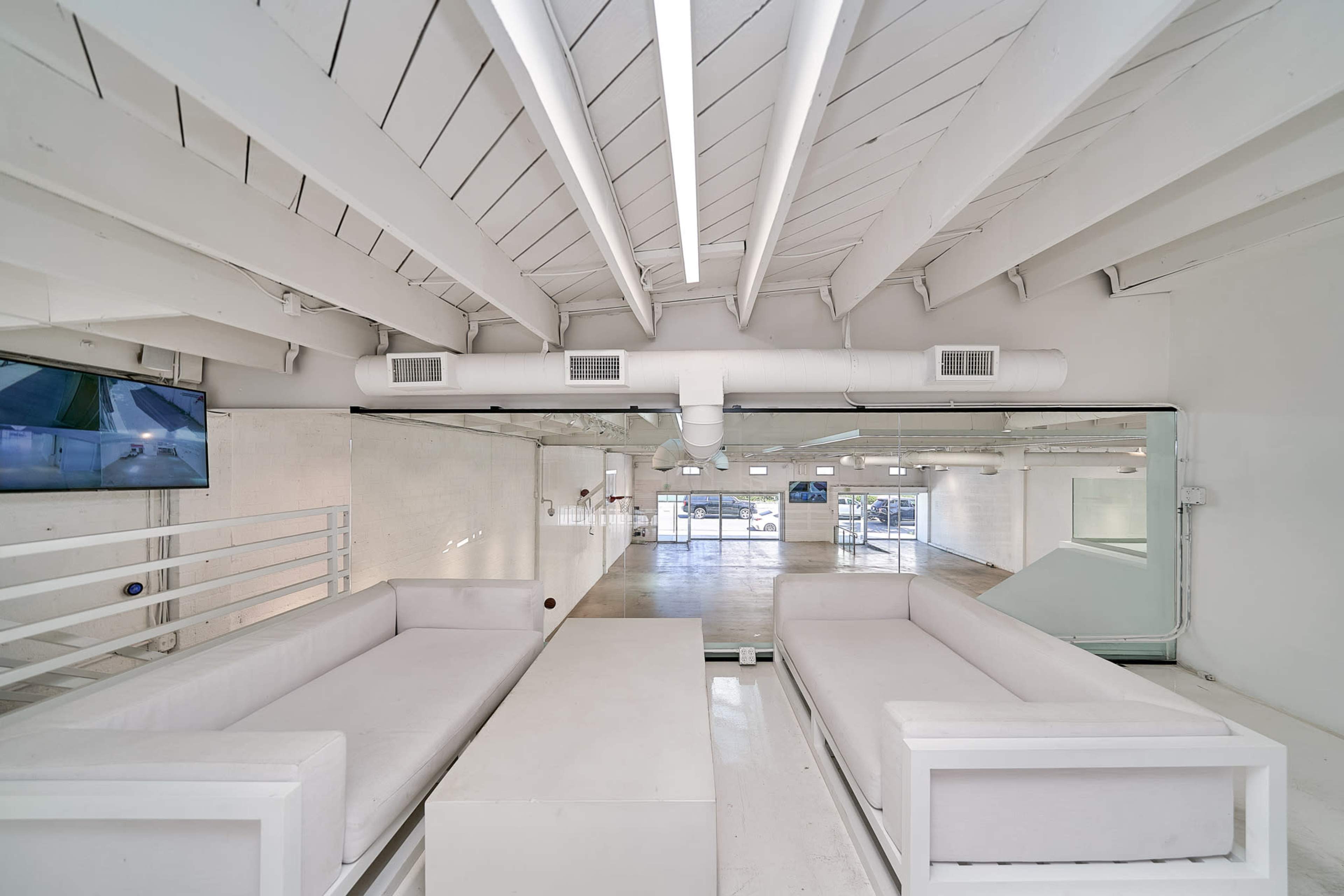 A minimalist interior space featuring white sofas and a coffee table, with exposed beams and large glass windows.