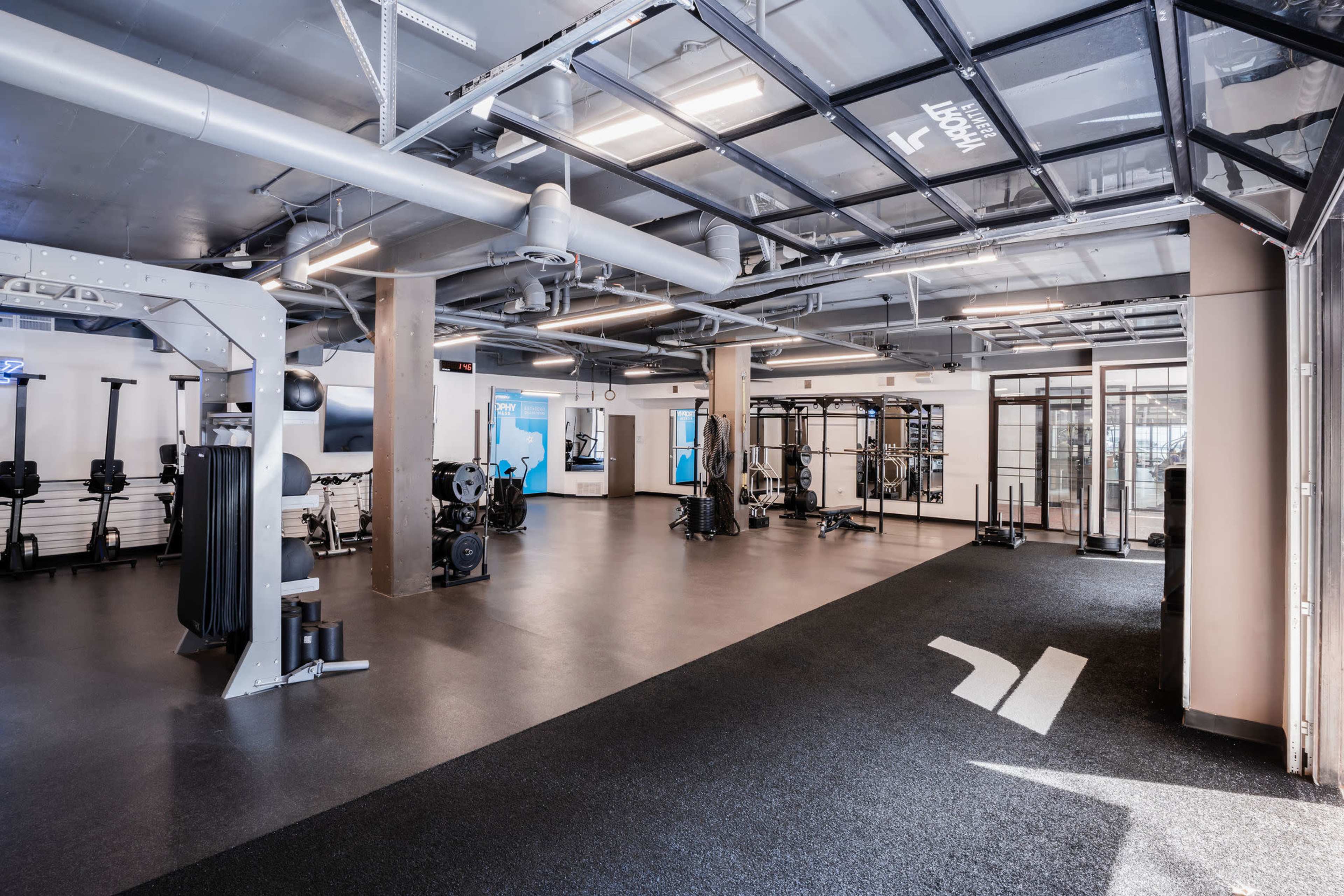 A spacious gym with various exercise equipment and a black rubber flooring.