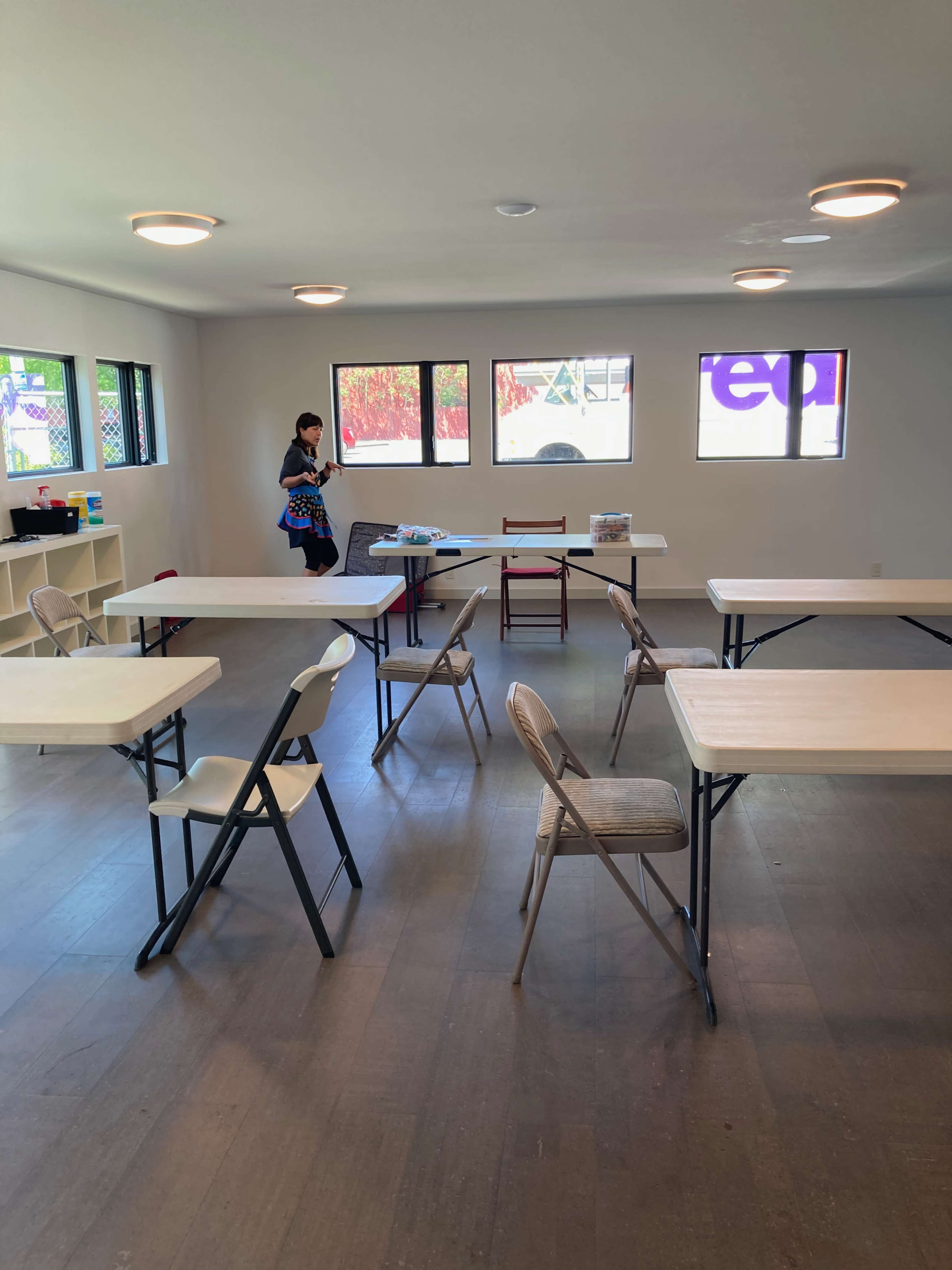 A person stands in a sparsely furnished room with several tables and chairs arranged in a neat configuration.