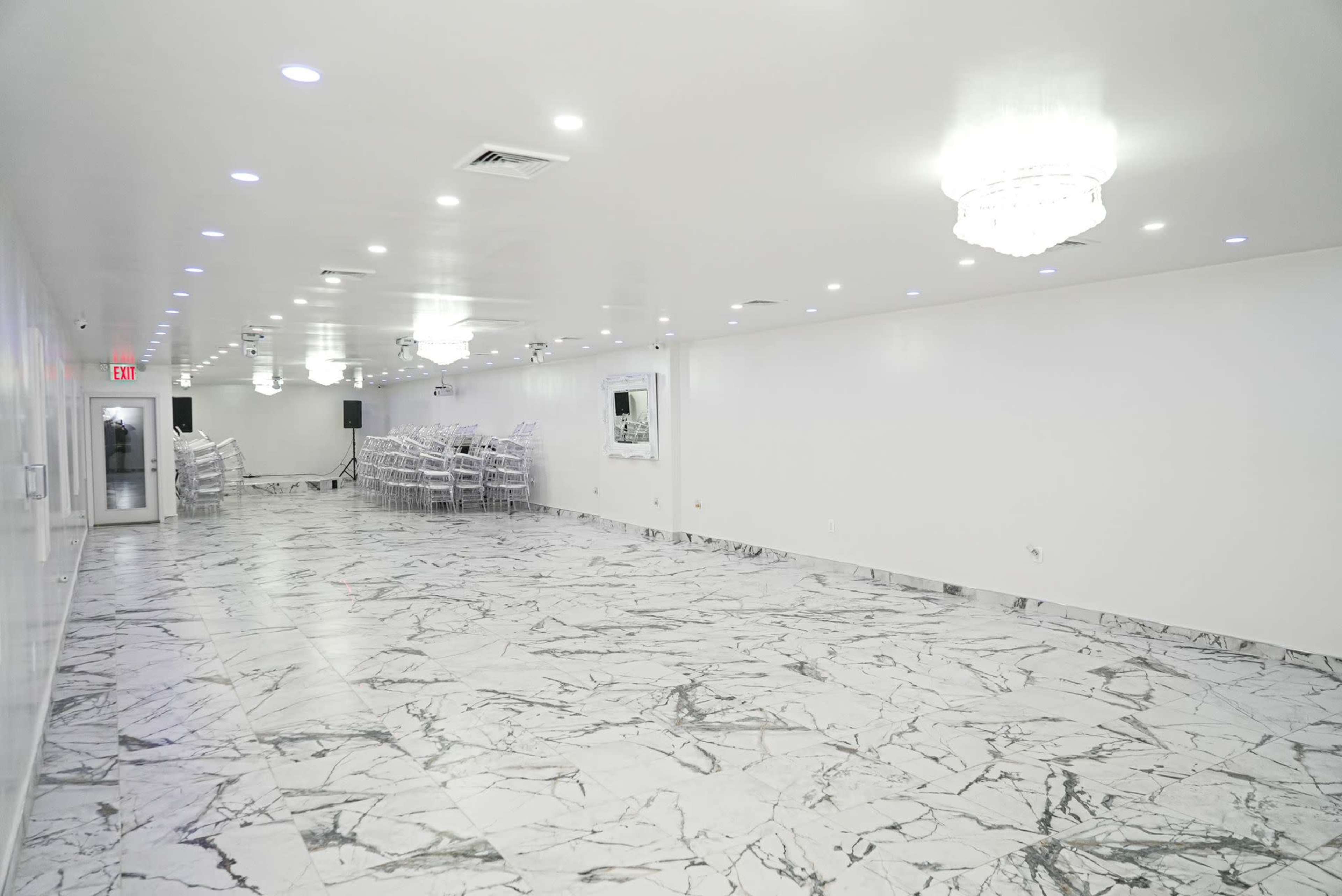 The image shows a spacious, empty room with white walls, marble flooring, and several illuminated chandeliers.