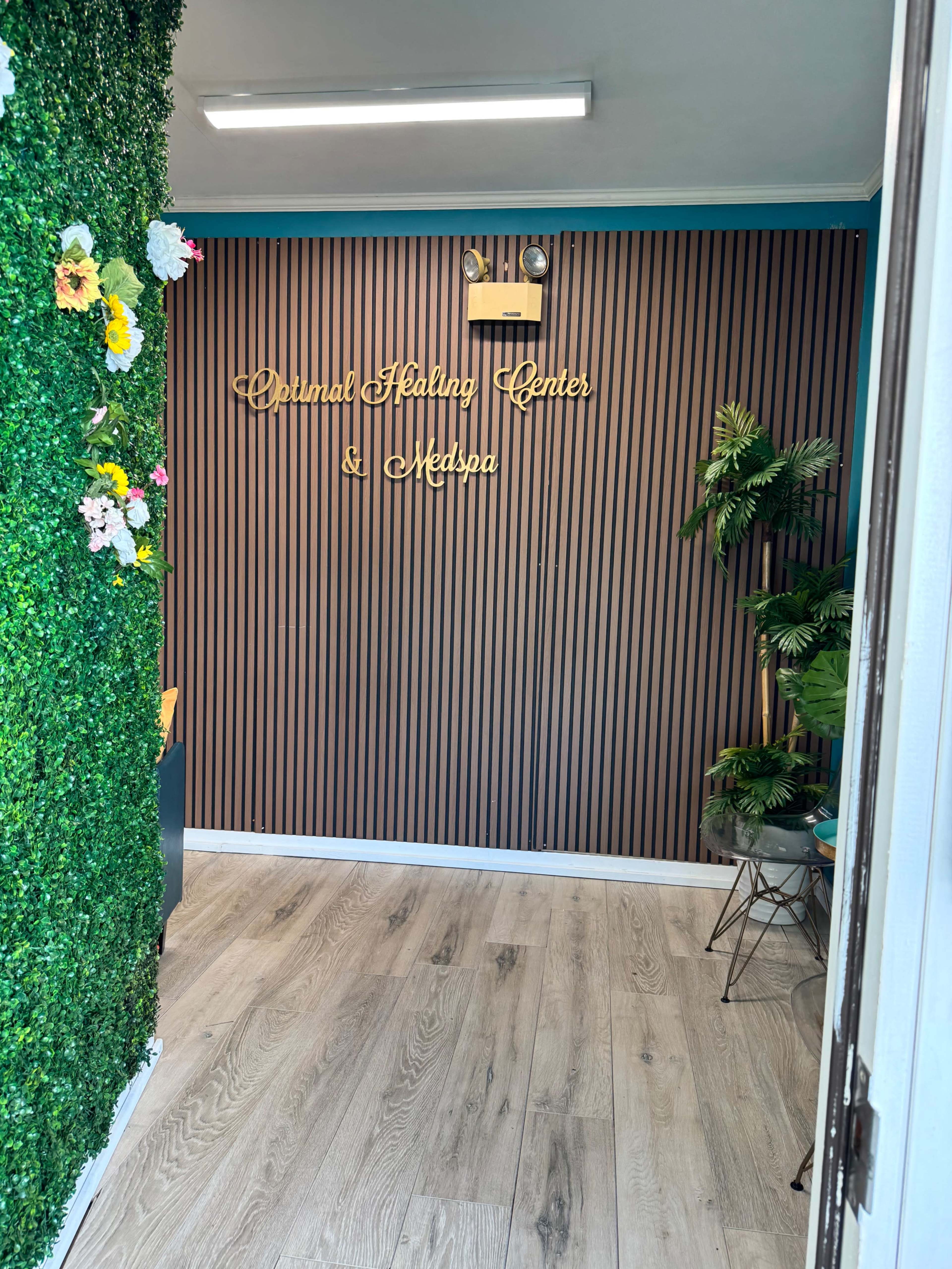 The image shows the interior of a wellness center with a wall featuring vertical stripes and decorative greenery, including flowers, alongside the sign for "Dermal Healing Center & Medspa."