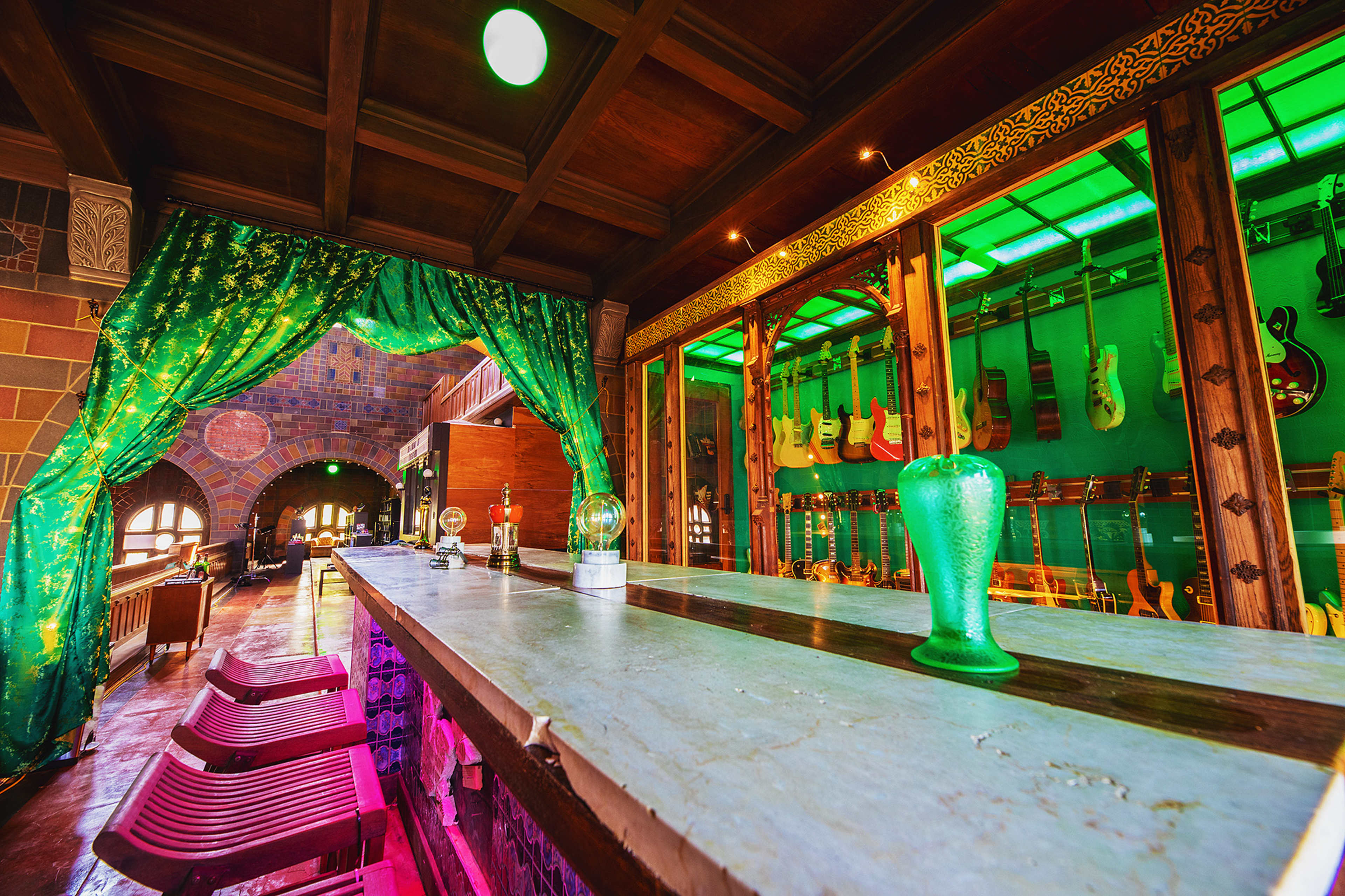 The image shows a dimly lit bar area with a green curtain, a stone counter, and a display of guitars in the background.