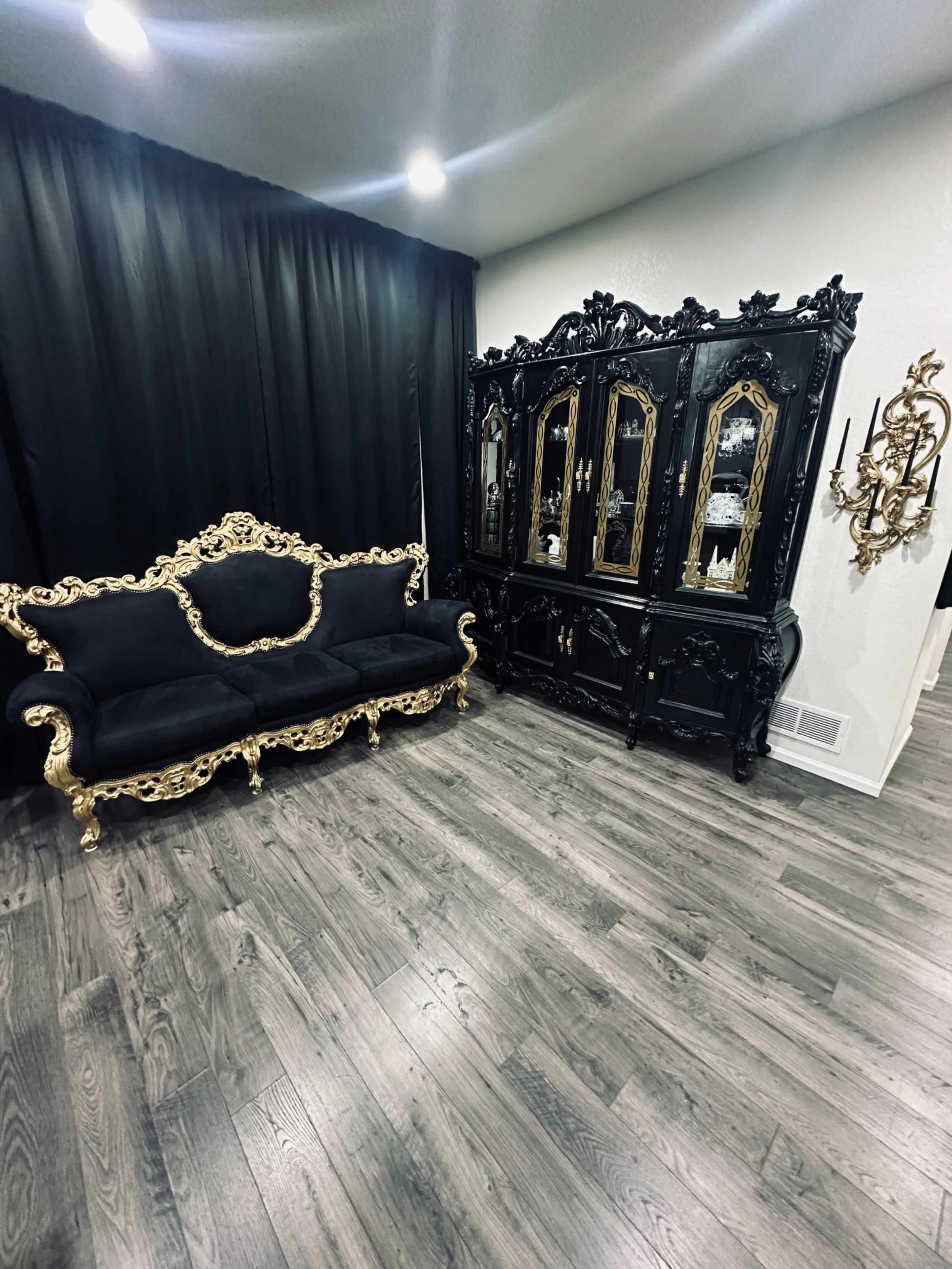 A dark room featuring an ornate black and gold sofa alongside a matching antique-style cabinet with mirrors.