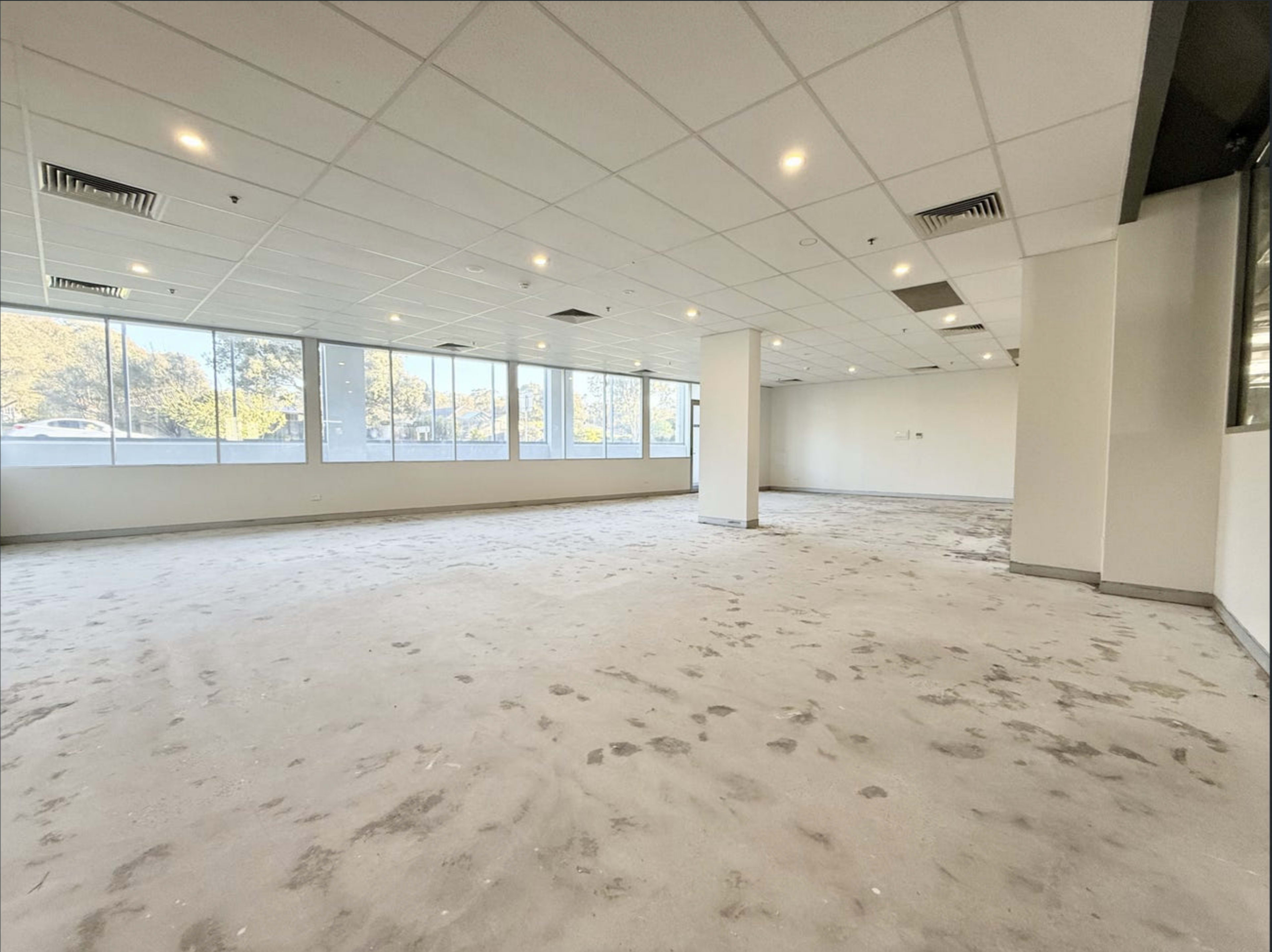 The image shows a spacious, empty office interior with large windows allowing natural light to enter.