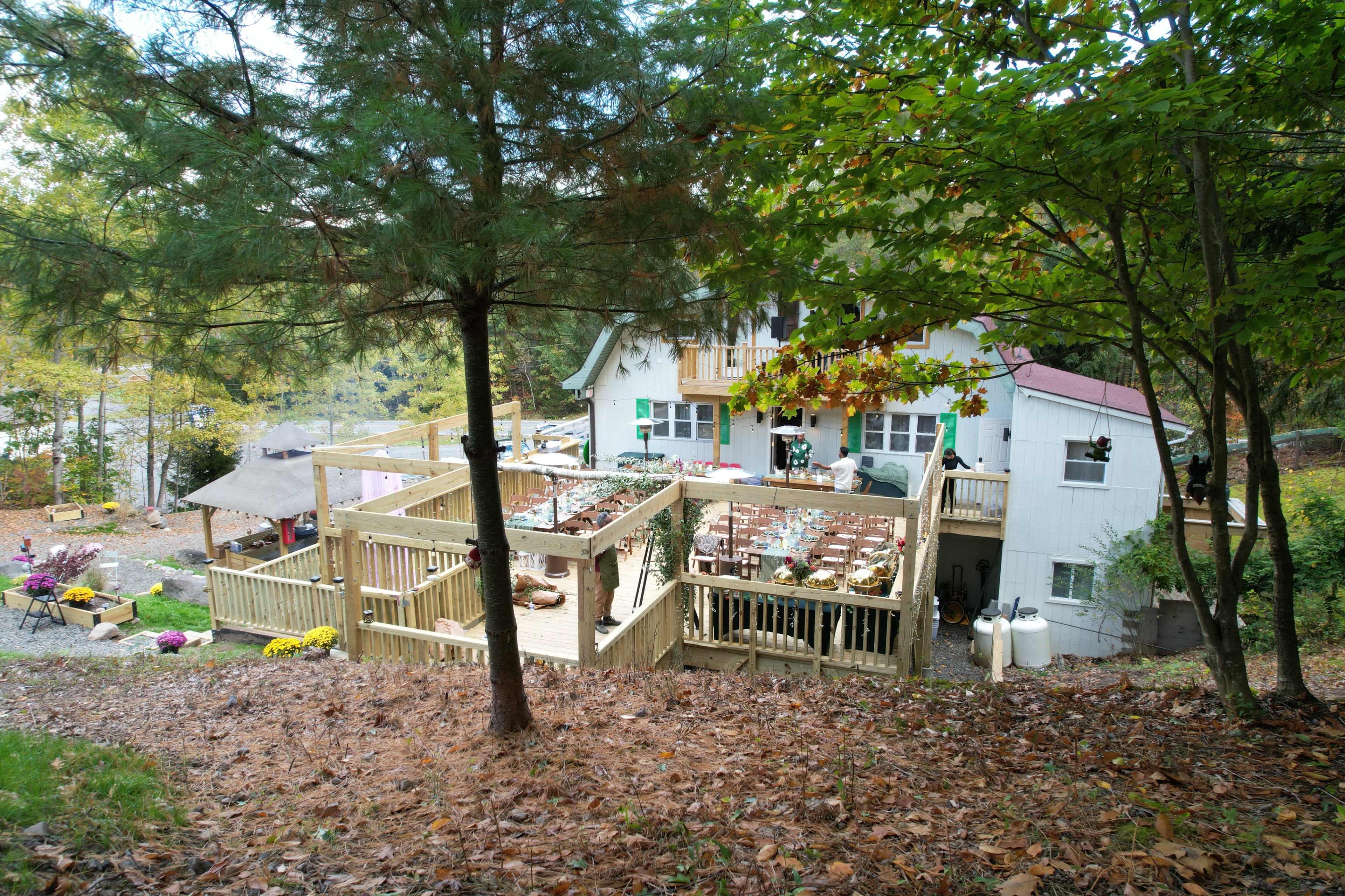 A two-story house surrounded by trees features multiple wooden decks with outdoor seating and decorated tables.
