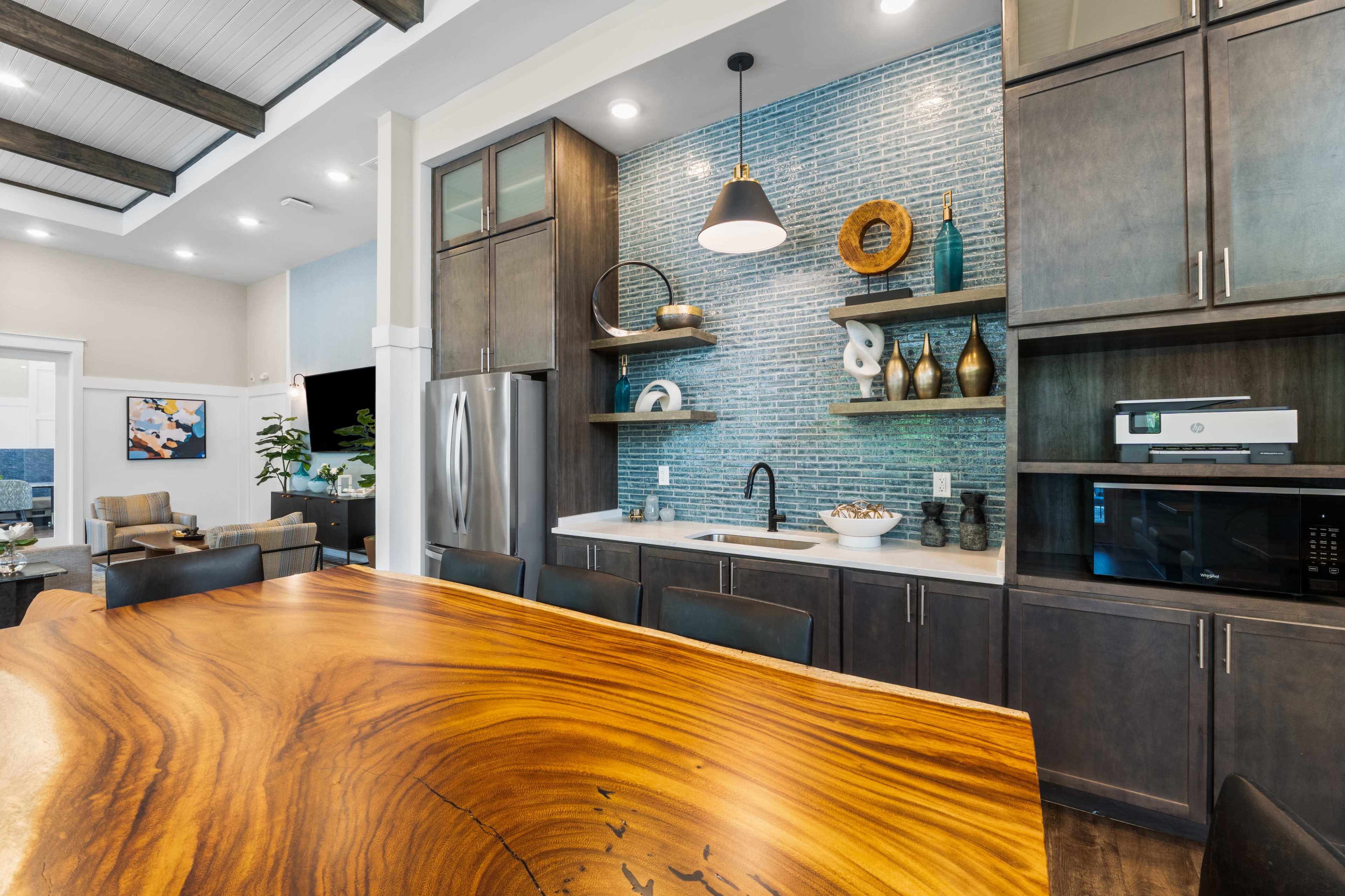 The image features a modern kitchen with dark cabinetry, a large wooden dining table, and a decorative backsplash made of blue tiles.
