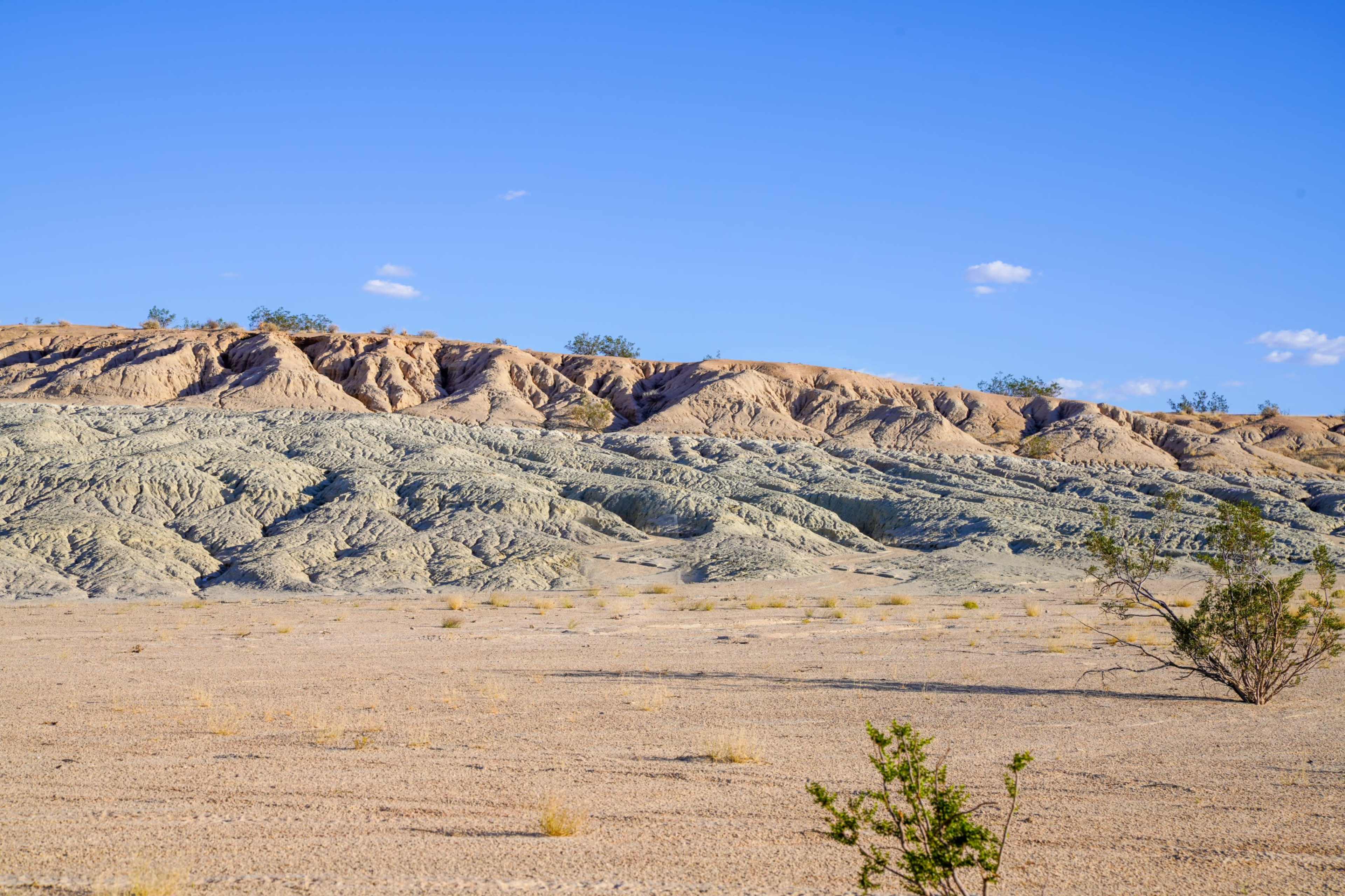 The image shows a barren desert landscape with layered, textured hills under a clear blue sky.