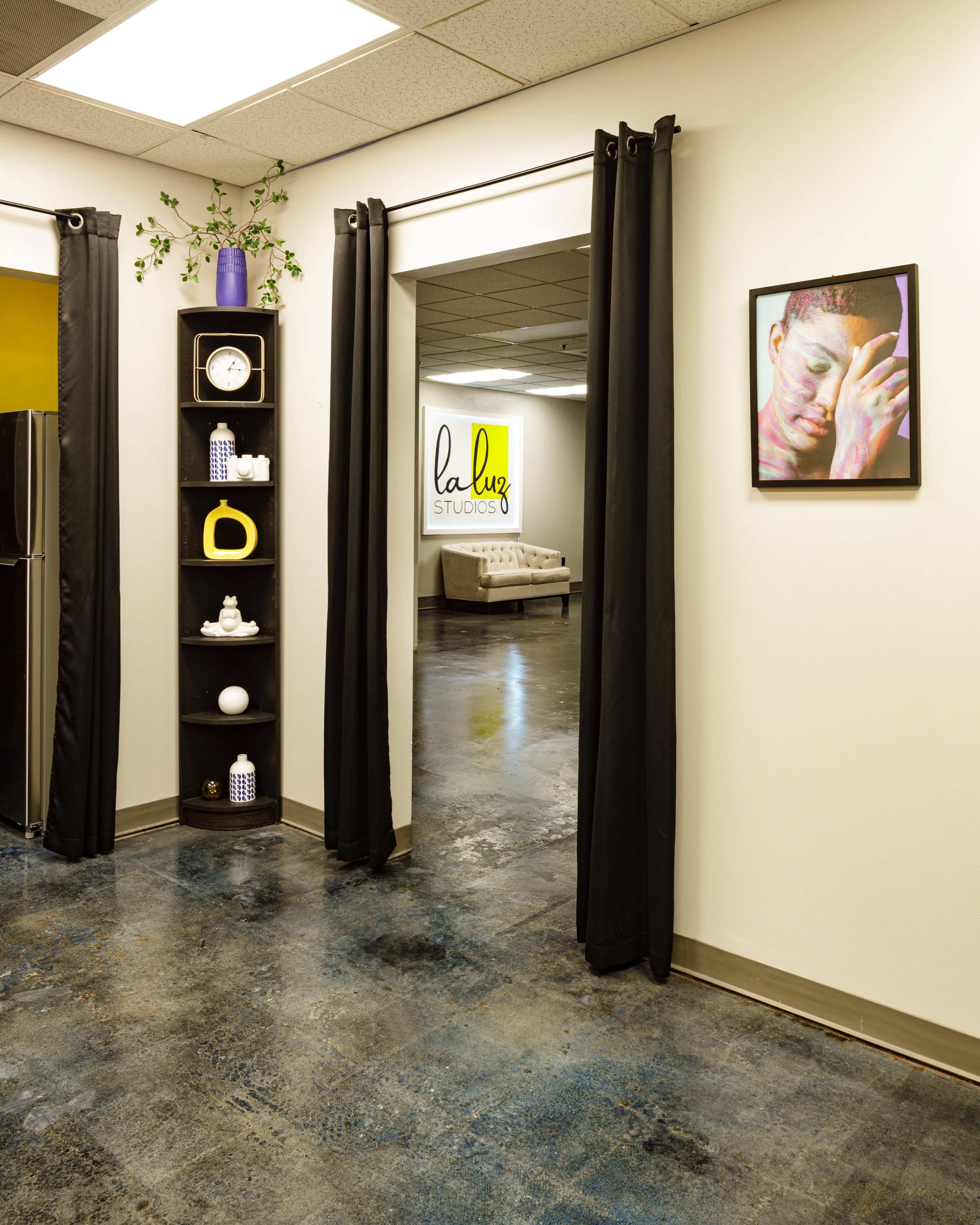 An interior space featuring a hallway with black curtains, a shelf displaying various objects, and a framed artwork on the wall.