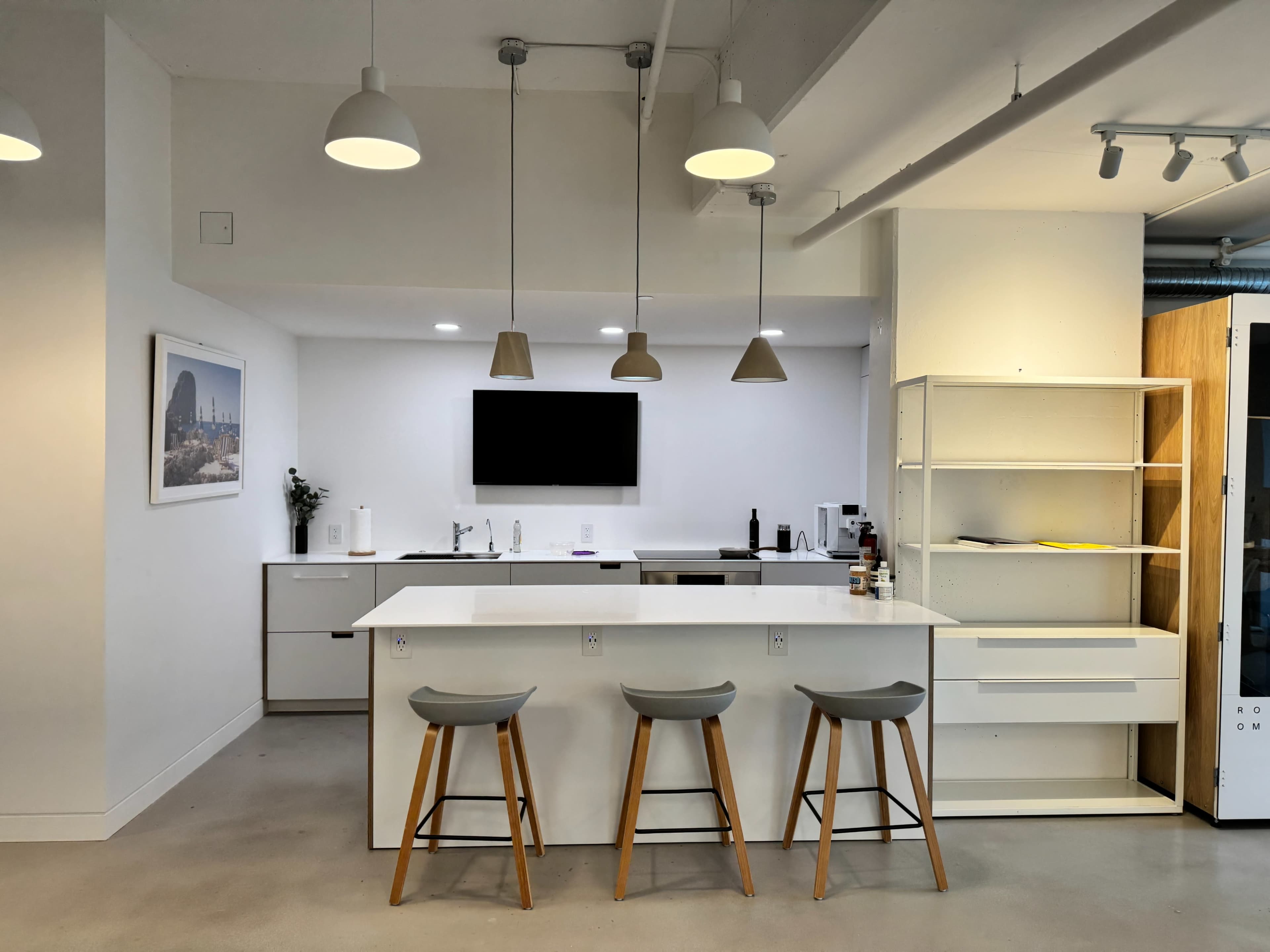 A modern kitchen with a central island and three stools, featuring white cabinetry and pendant lighting.