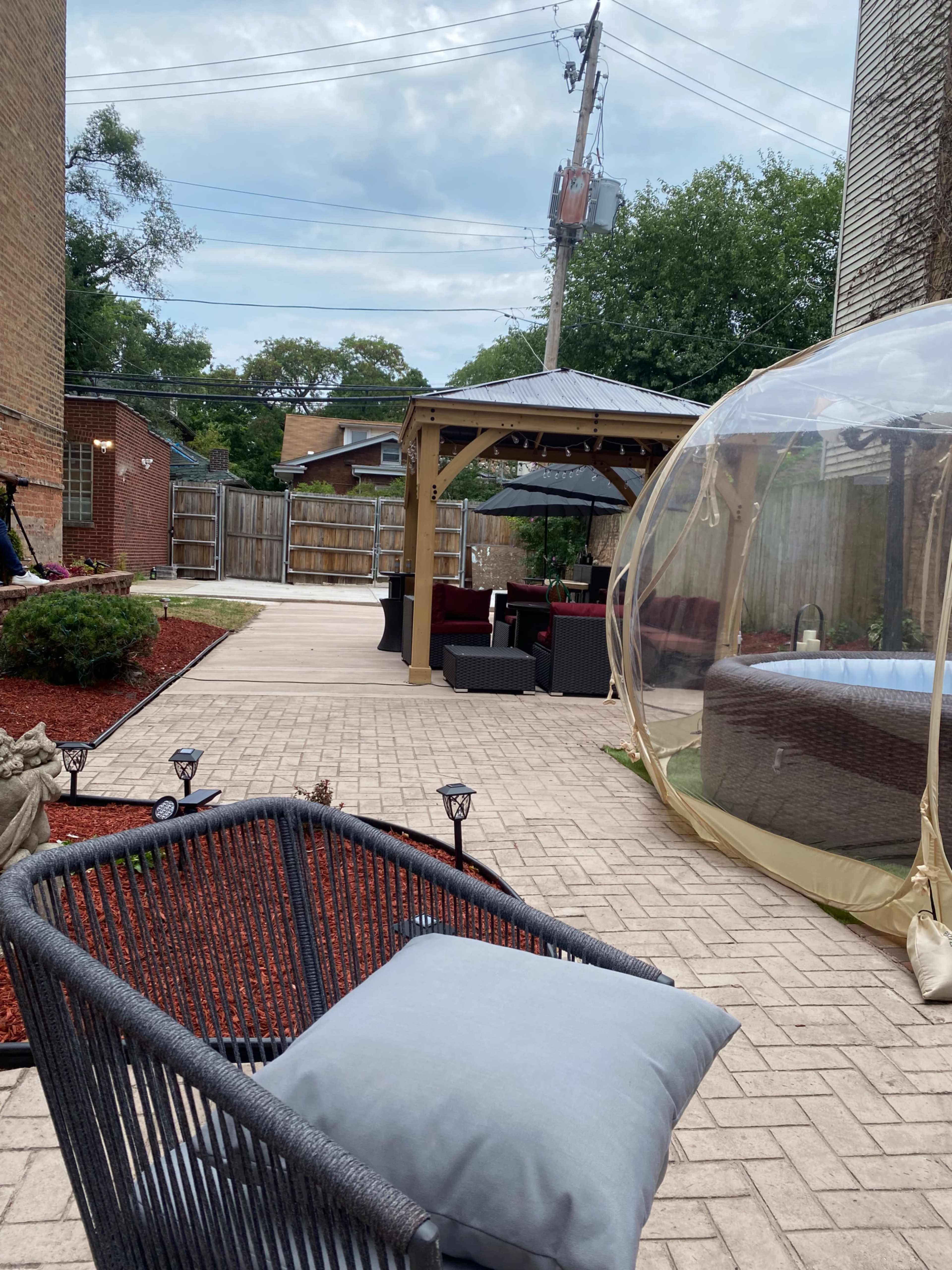 A landscaped backyard with a gazebo, a transparent dome structure, and seating arrangements on a paved patio.