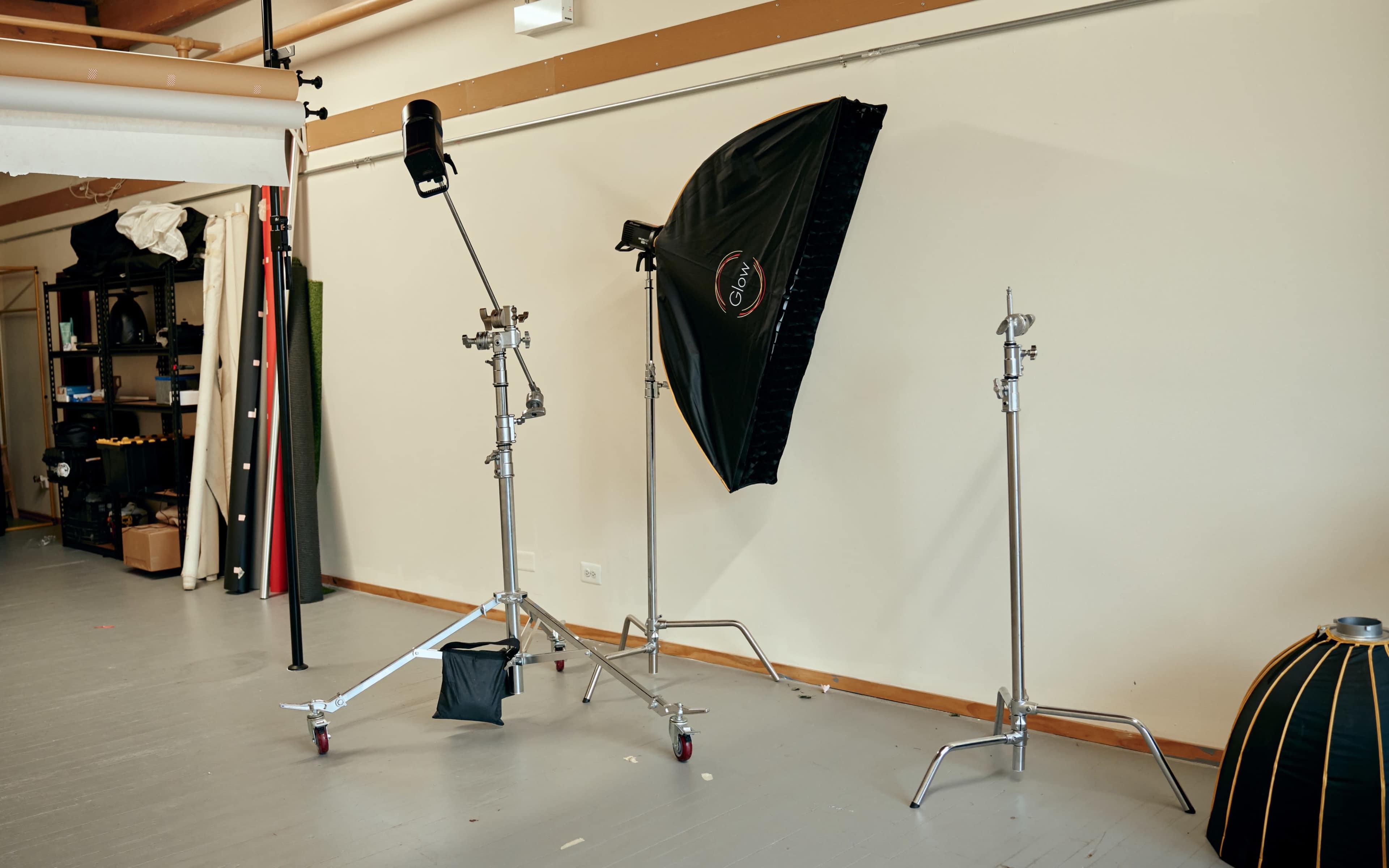 The image shows a photography studio setup with light stands, a softbox, and various backdrops along the wall.