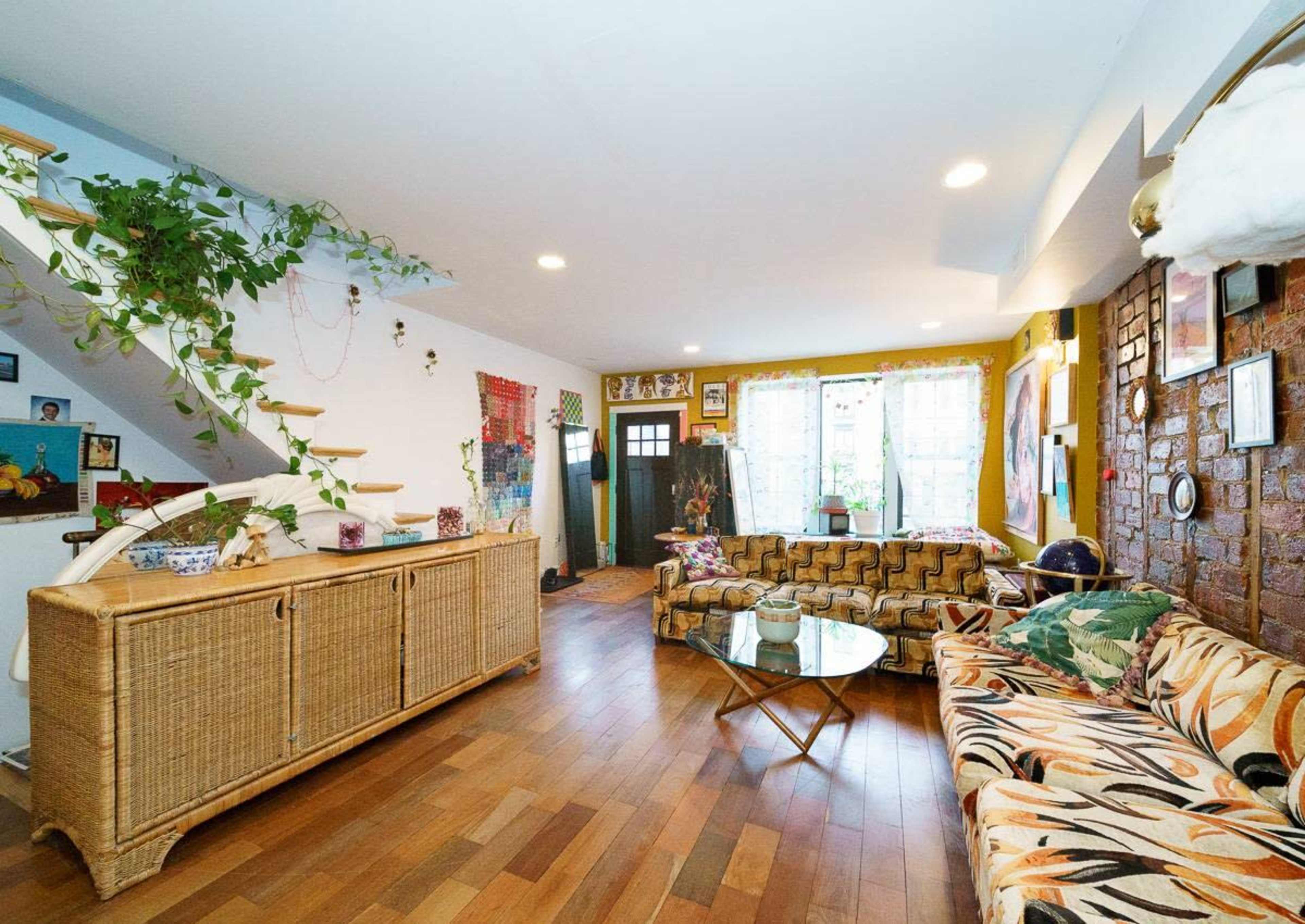 A spacious living room with a staircase, rattan furniture, a glass coffee table, and various wall decorations.