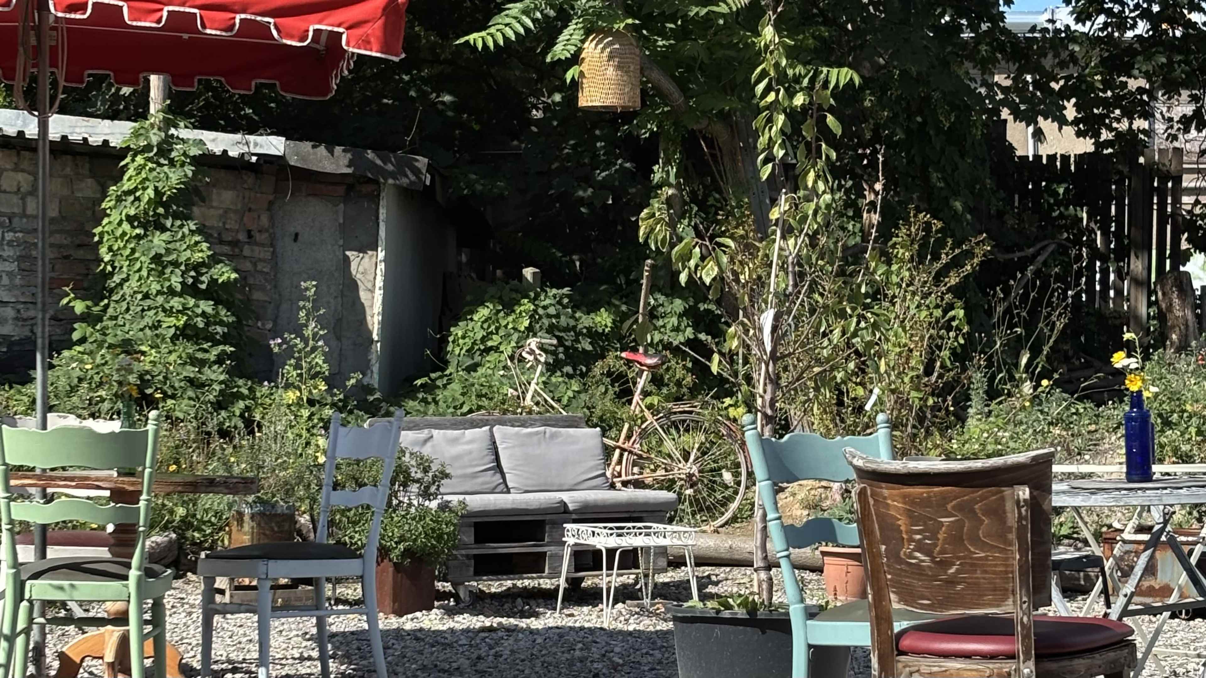 The scene displays an outdoor seating area with various chairs and a gray sofa surrounded by greenery and a vintage bicycle in the background.