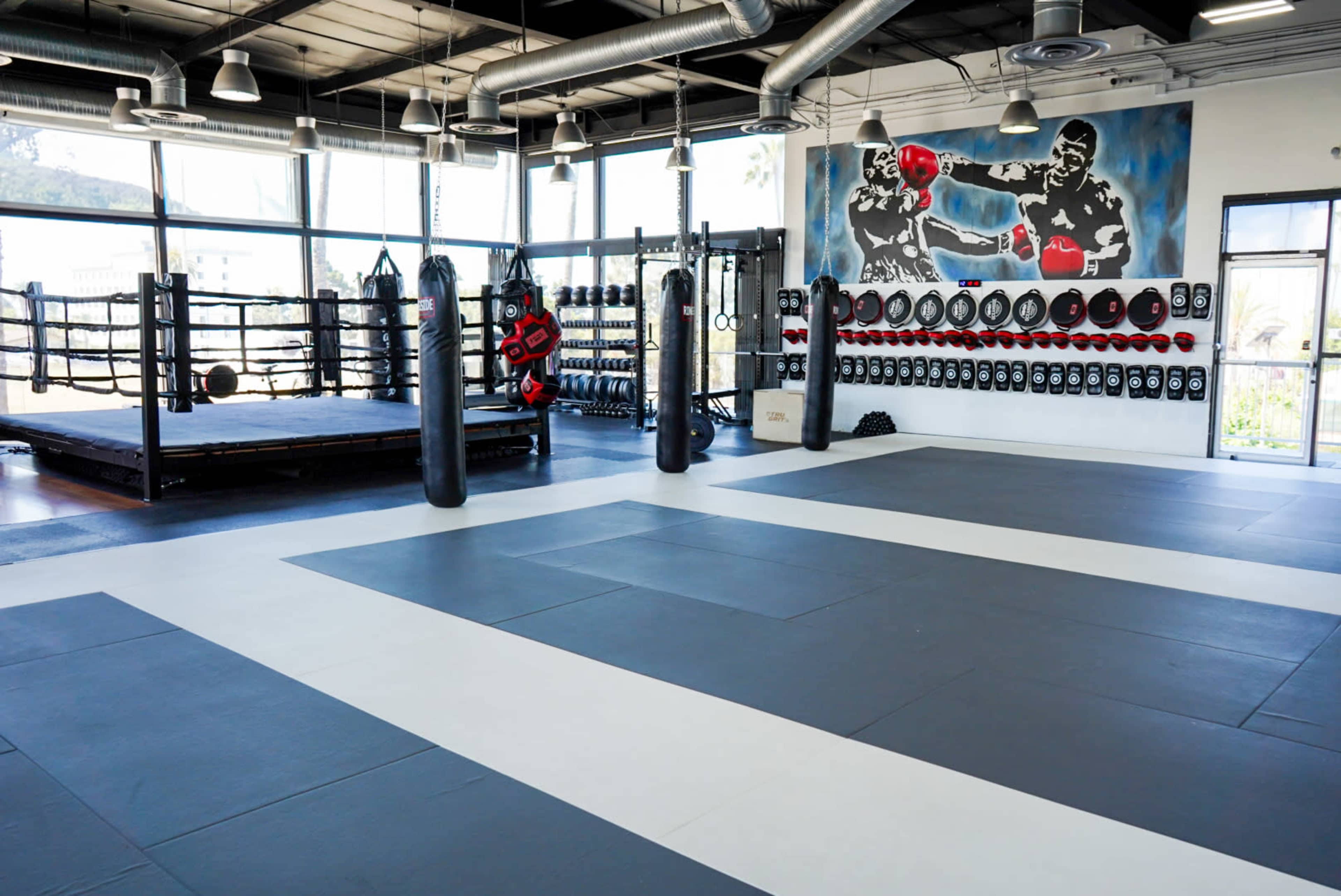 A spacious training facility with boxing rings, punching bags, and a wall decorated with boxing gear.