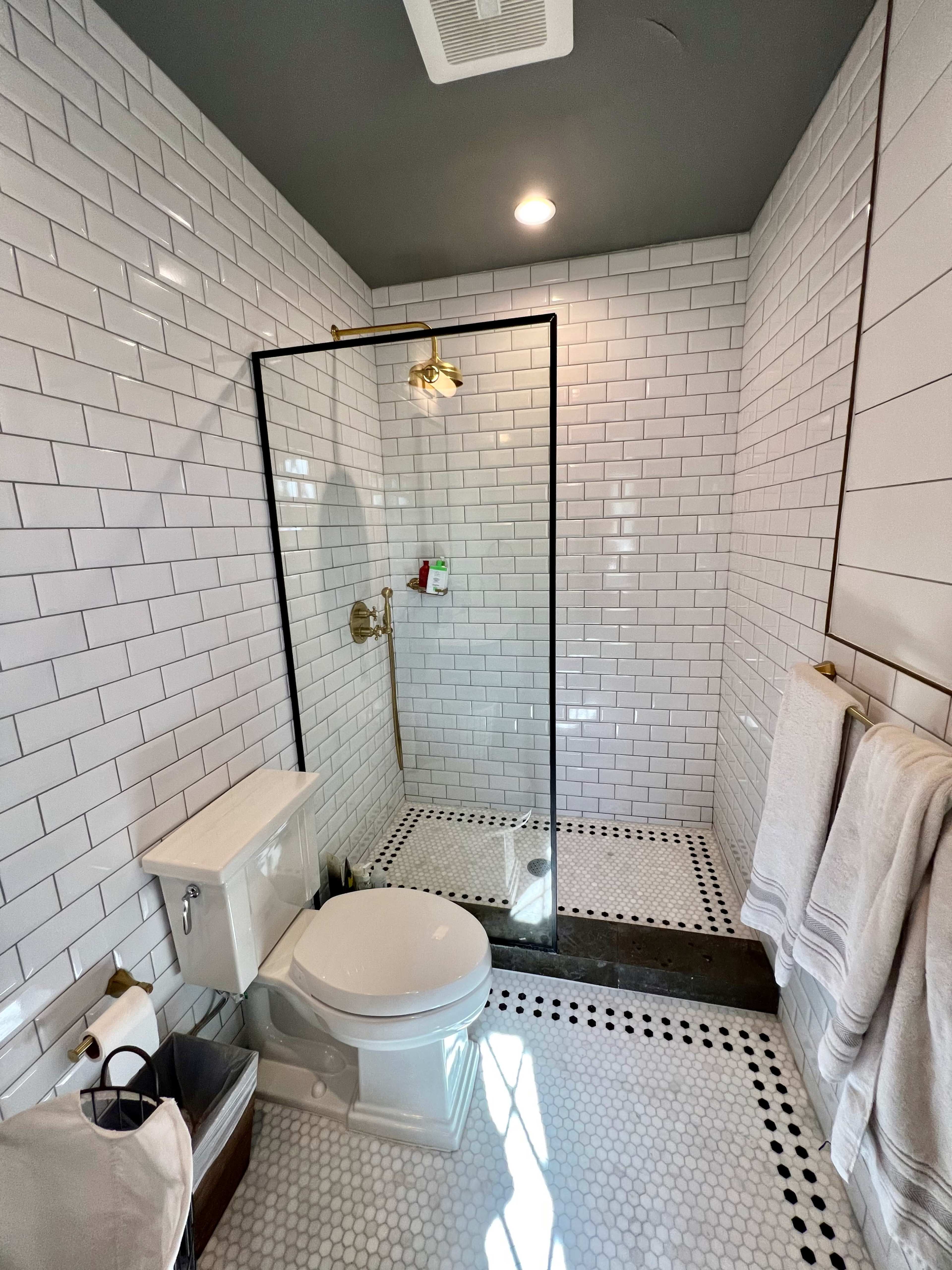 A bathroom with white subway tile walls, a glass shower enclosure, a toilet, and a hexagonal tiled floor.